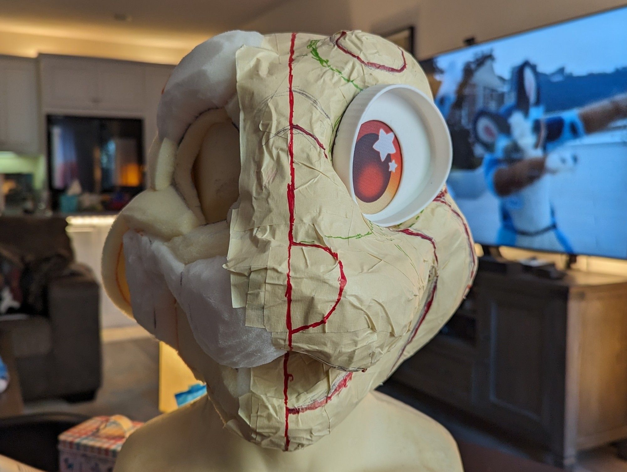 A frontal photo of Satchel's new fursuit head as a foam base, with tape and markings drawn on it. A "follow-me" eye is placed for reference.