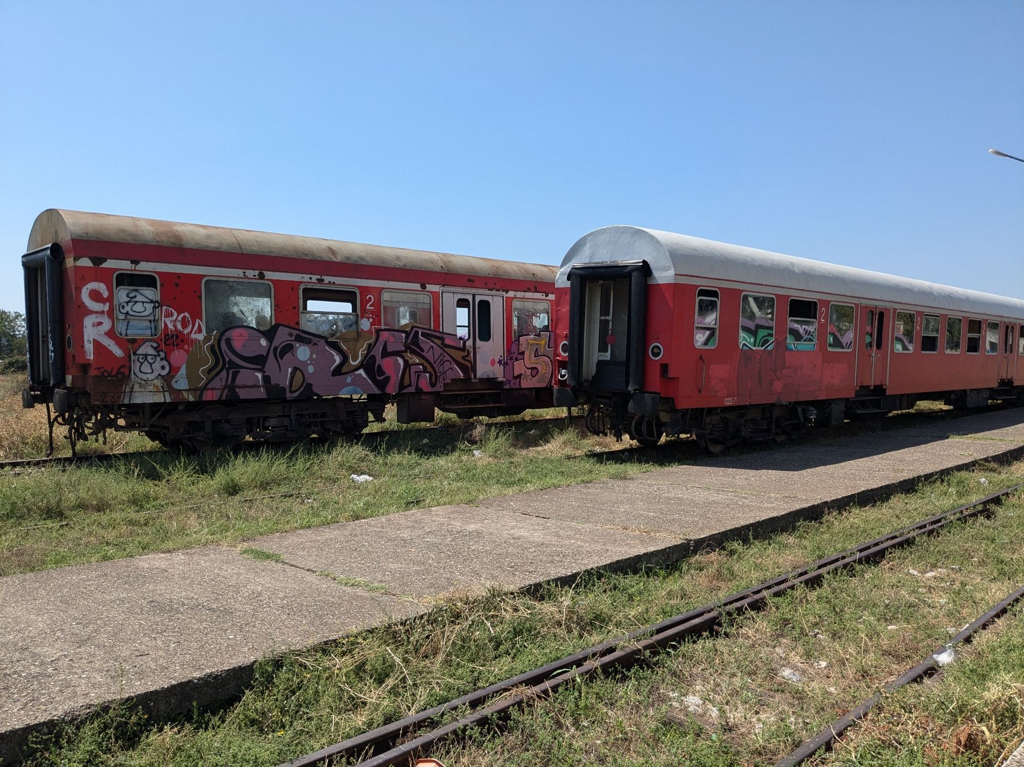 Im Bahnhof stehen zwei Garnituren mit alten Ex-Silberlingen von DB-Regio. Die meisten Scheiben sind zertrümmert oder fehlen ganz. Wer es nicht glauben will: Es gibt Videos auf YouTube, in denen zu sehen ist, dass dieser Zug tatsächlich fährt.