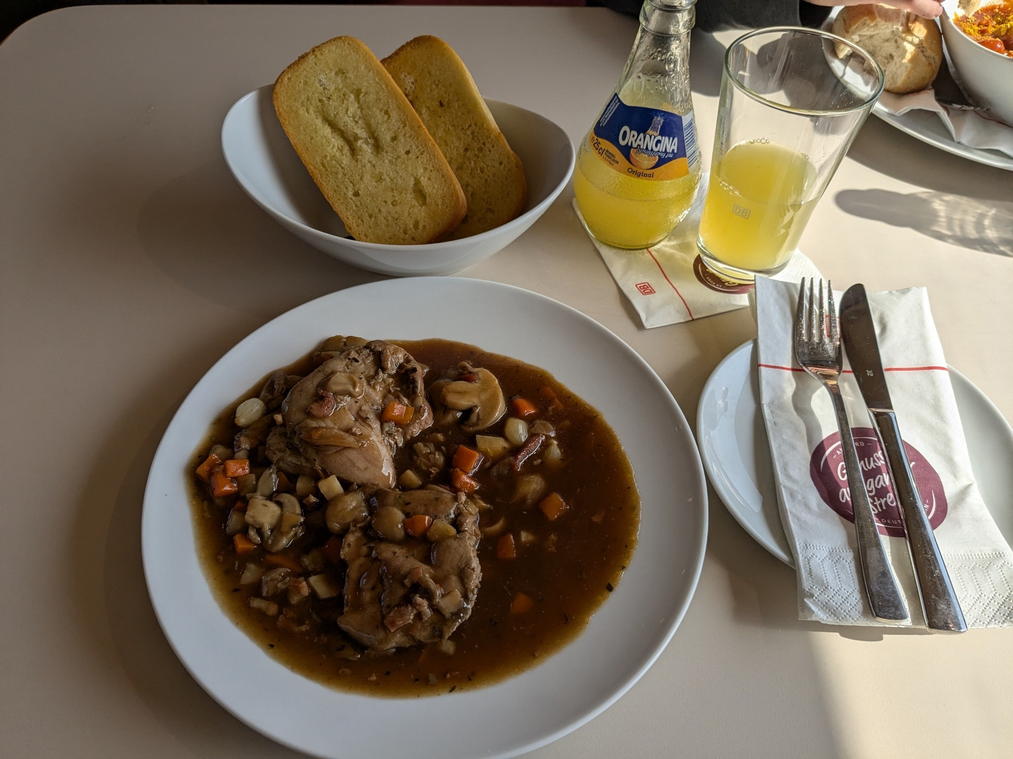 Ein Teller Coq au vin, Knoblauchbrot und Orangina im Bordrestaurant des ICE