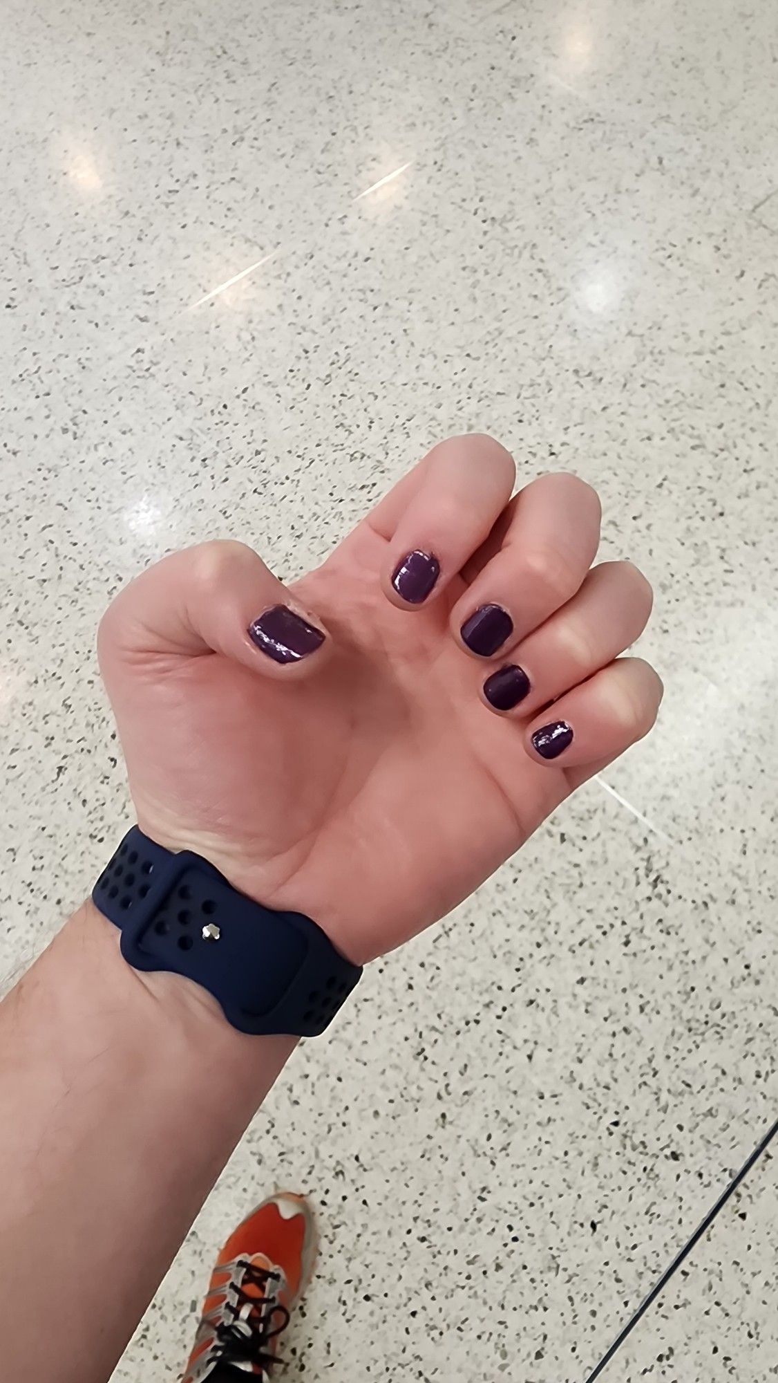 Left hand palm with curled fingers and purple nails, smartwatch, orange shoe in background