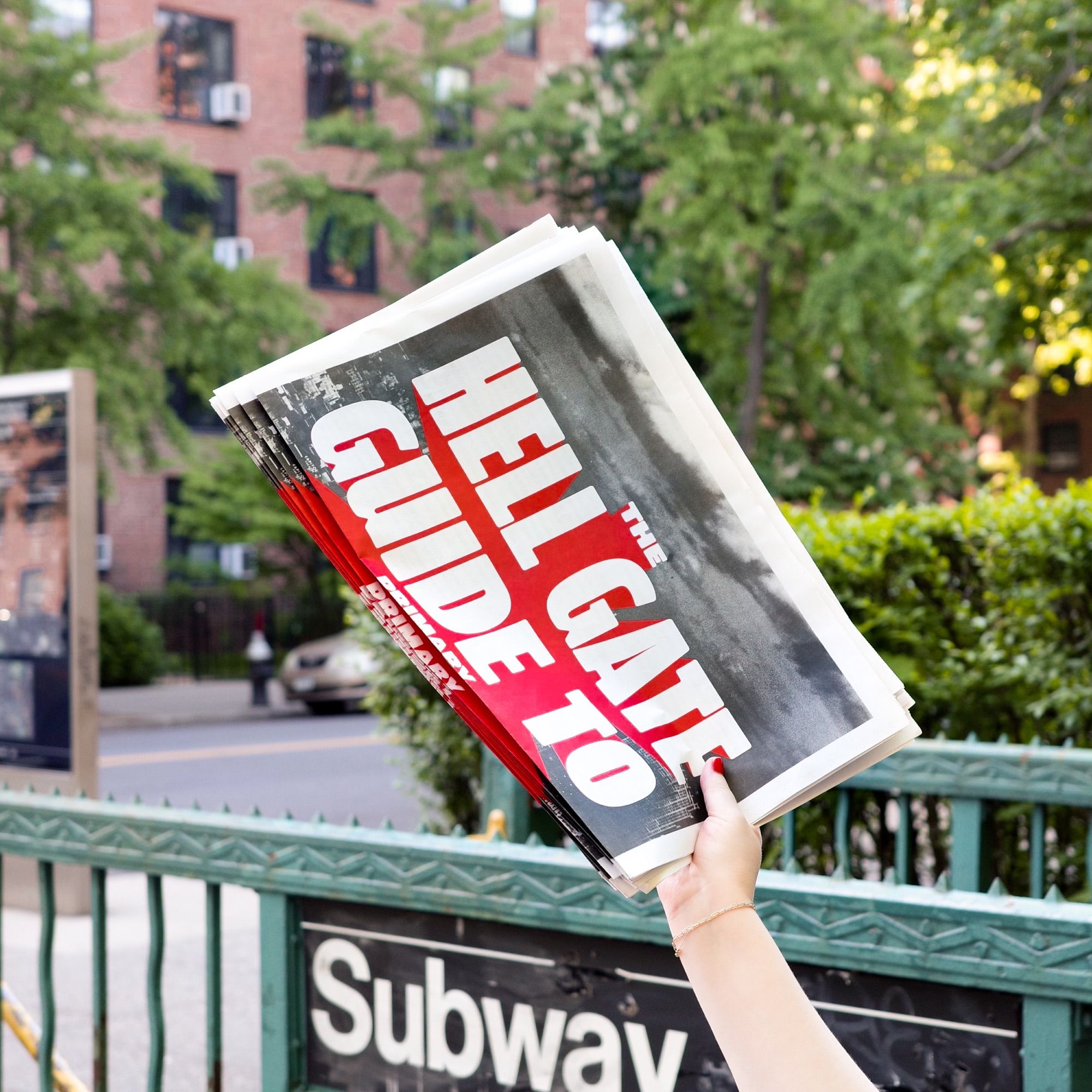 Photo of hand holding stack of newspapers outside of a NYC subway stop