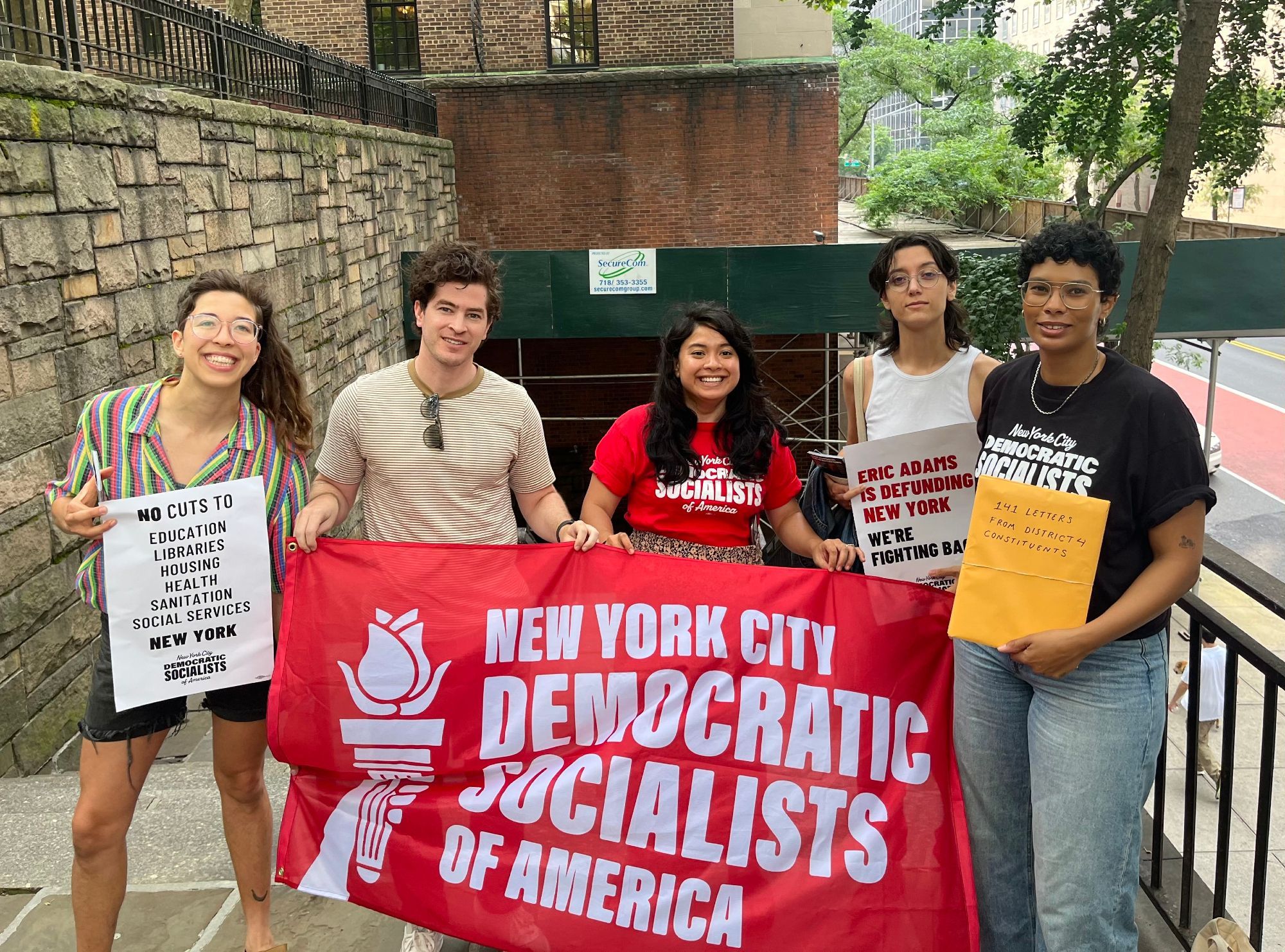 Group of people in NYC-DSA shirts holding a red flag reading "New York City Democratic Socialists of America" 