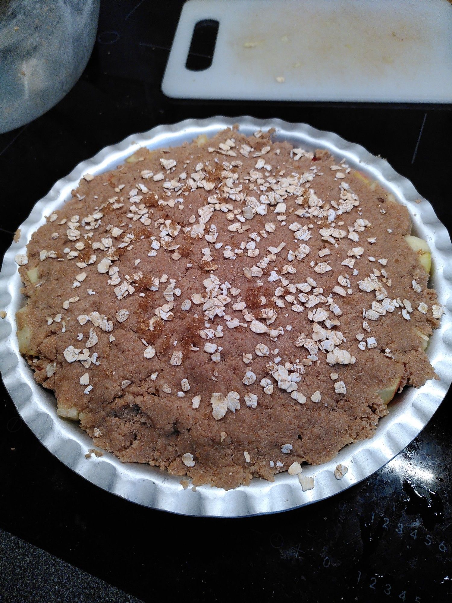 A metal dish with a crumble covering, a few bits of apple peeping out of the edge, sprinkled with oats and Demerara sugar.