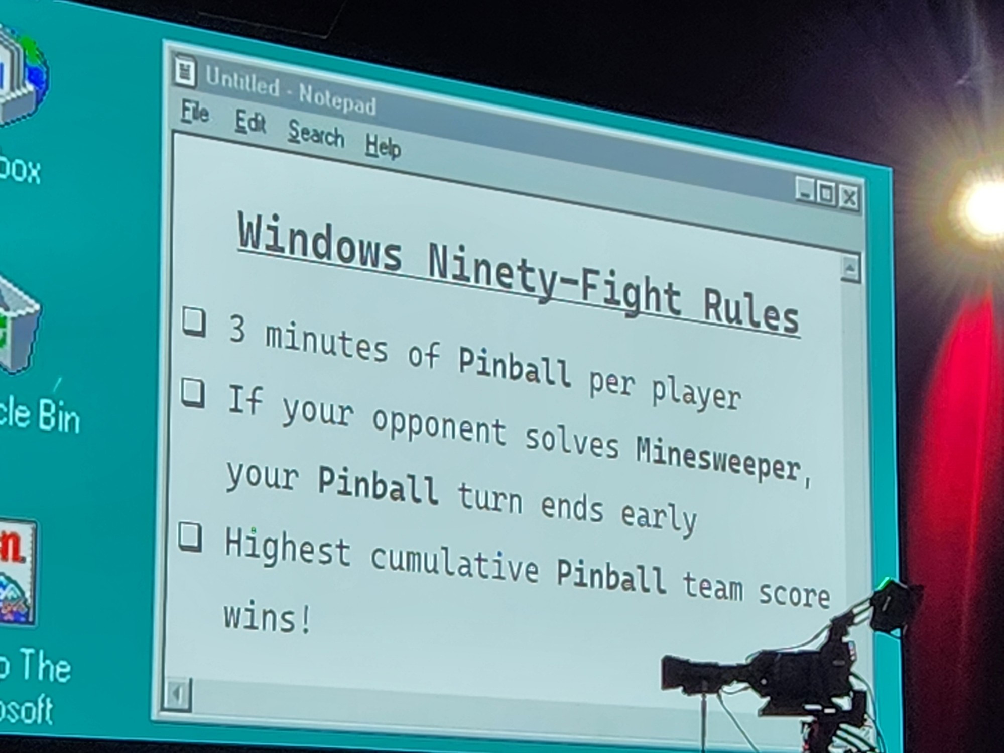 A 90s style desktop is projected with a notepad window open that reads "windows ninety-fight rules
3 minutes of Pinball per player
If your opponent solves minesweeper your Pinball turn ends early
Highest cumulative Pinball team score wins!"