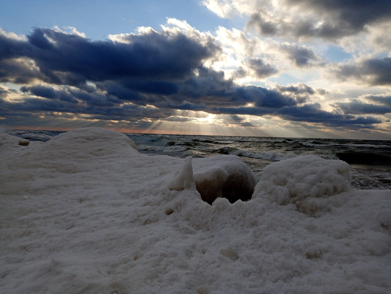 Lake Michigan with spectacular sun rays under the clouds and ice on the beach