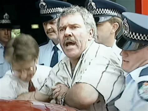 Jack Karlson, a white Australian man being guided into a police car by multiple police officers, at least one of whom by virtue of the quality of his headlock “knows his judo well”