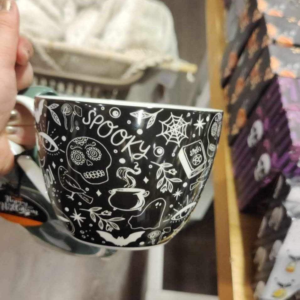 I am holding a mug with a Halloween-themed design (with skulls, spiderwebs, a cauldron, ghosts, bats, a spellbook etc) and the text spooky. In the end, I bought two of them.