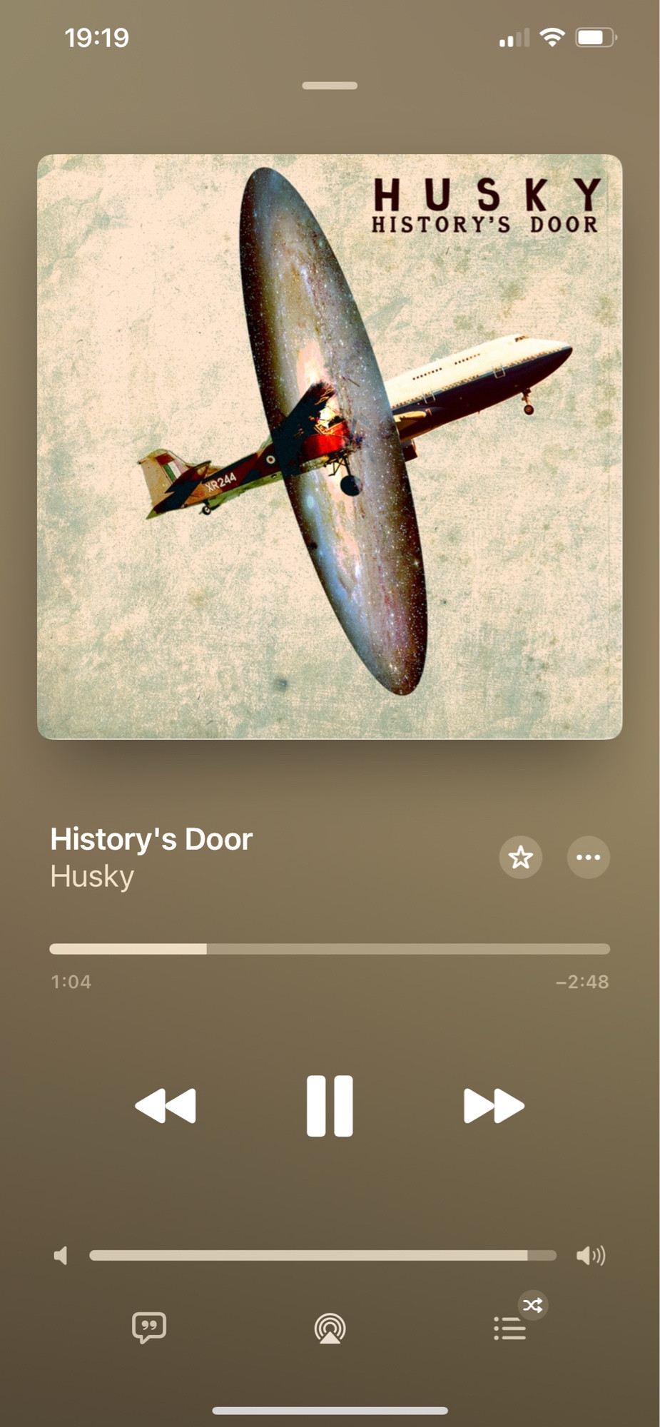 A screenshot of the Apple Music app with a song playing. The song is “History’s Door” by Husky. The album art shows a plane passing through a portal, one half an old biplane, the other half a new modern jet.