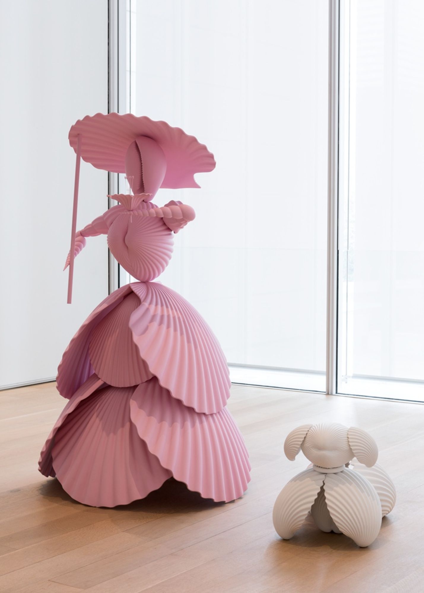 Katharina Fritsch makes meticulous reproductions of everyday objects, rendering them unfamiliar through extreme shifts in scale and bold color choices, both alluring and repellent. Indeed, saturated and nonreflective coats of color lend her sculptures a strong sense of otherworldliness. The marvelously pink <em>Woman with Dog</em> is clearly scaled up—enormously so—from a small figurine made of shells, as one might find in a seaside souvenir shop.