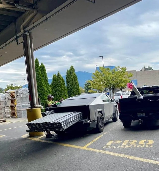 a man packing loose beams into the "bed" of his cybertruck. The gate is down.