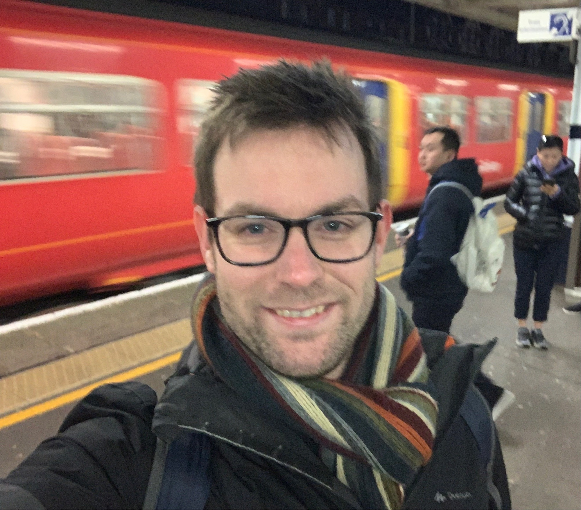 A sleepy morning selfie from a train station platform with a moving train in the background