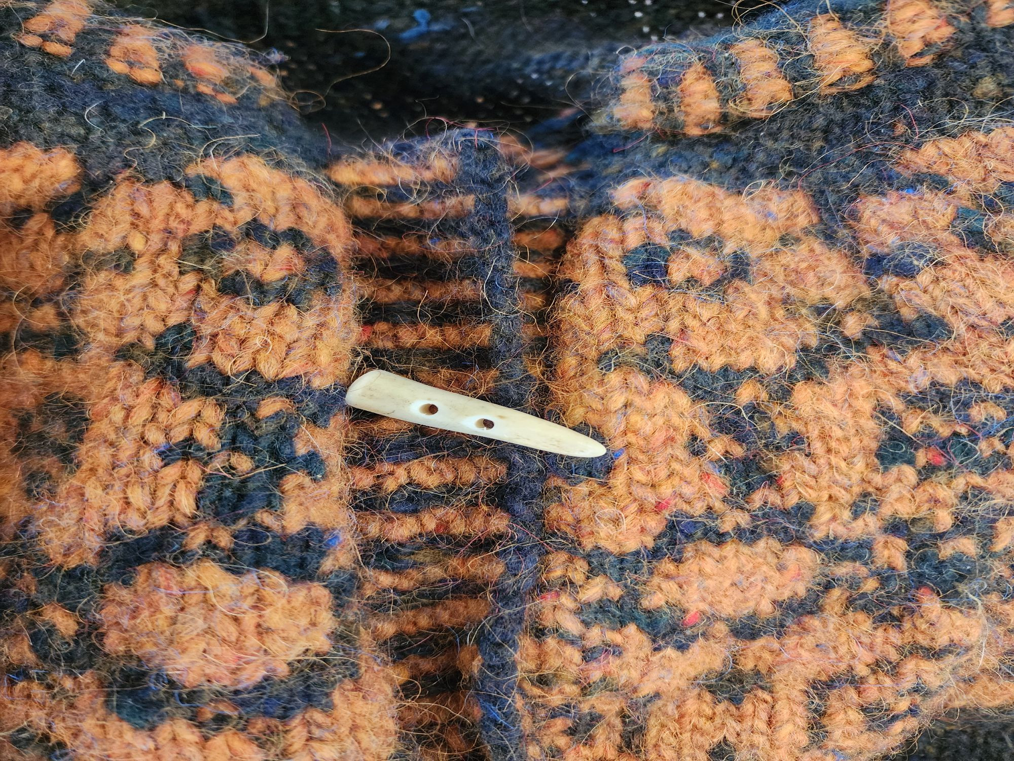 a beautiful two-hole button made from a polished deer antler tip rests on a cardigan sweater, waiting to be sewn into place. 