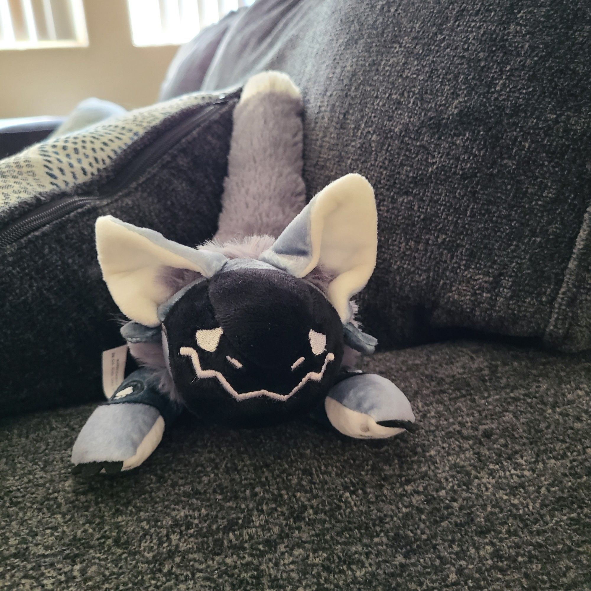 A "gloomy protobean" sits on a couch. It is grey with a gloomy face on its visor!