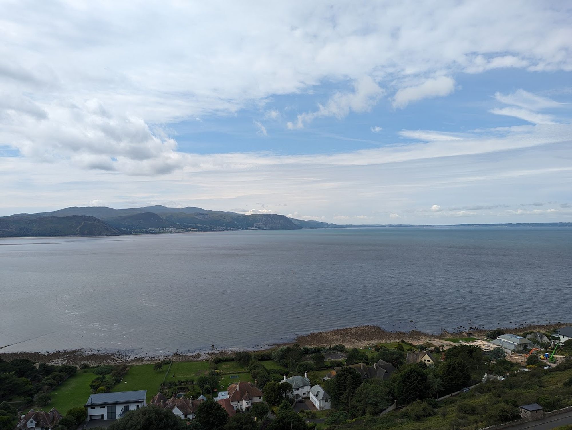 A view of a sea with hills in the distance and houses at the bottom.