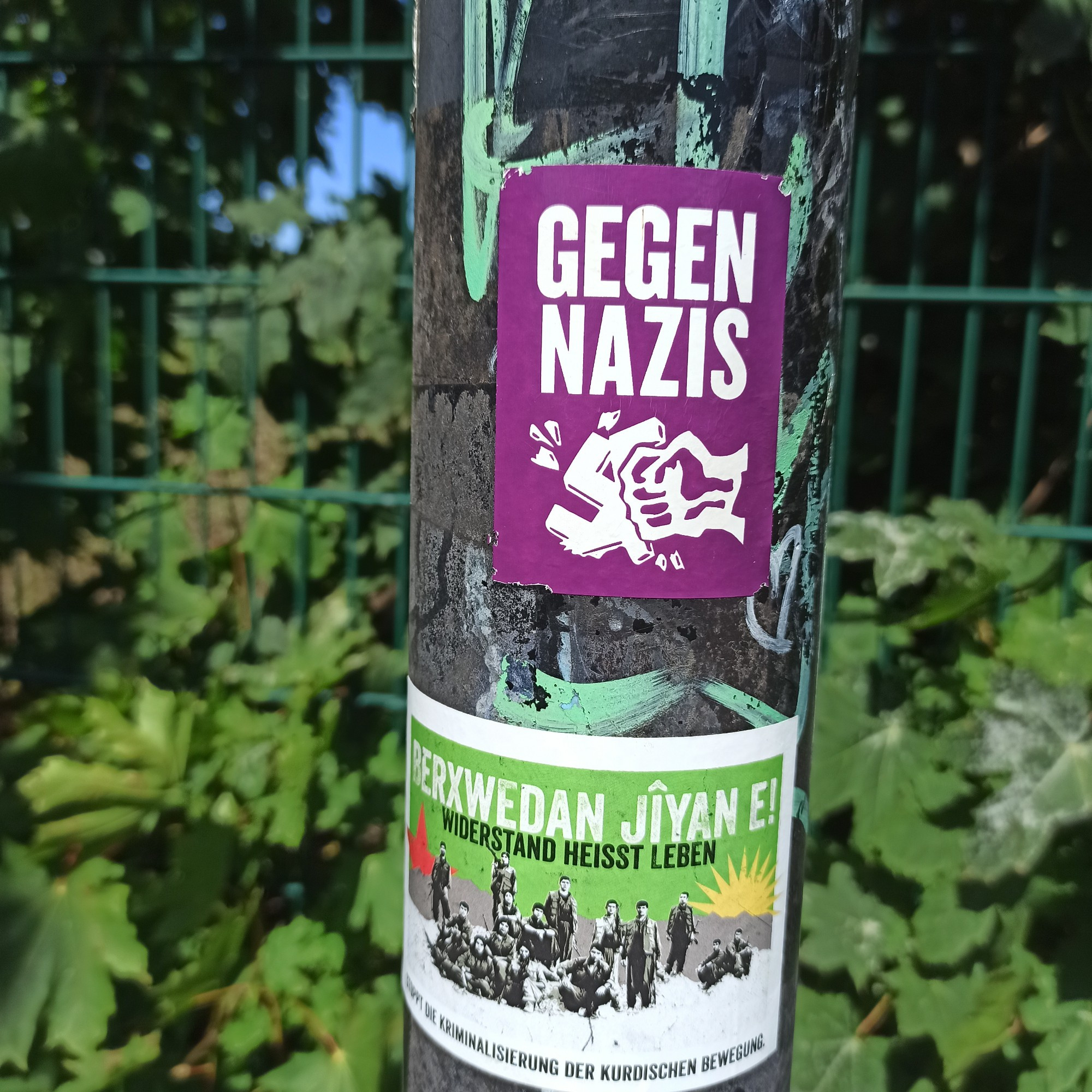 Antifa Sticker in pink auf Laternenmast. Zu sehen ist eine Faust die ein Hackenkreuz zerschlägt. Zu lesen ist gegen Nazis