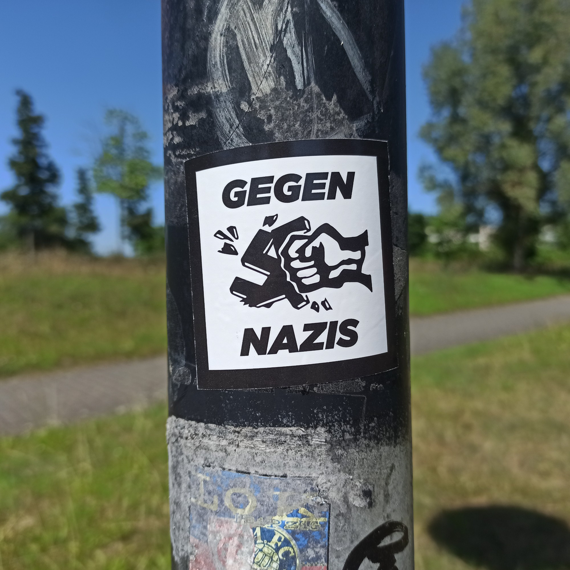 Antifa Sticker an Laterpfhal. Zu sehen ist eine Faust die ein Hackenkreuz zerschlägt. Zu lesen ist Gegen Nazis