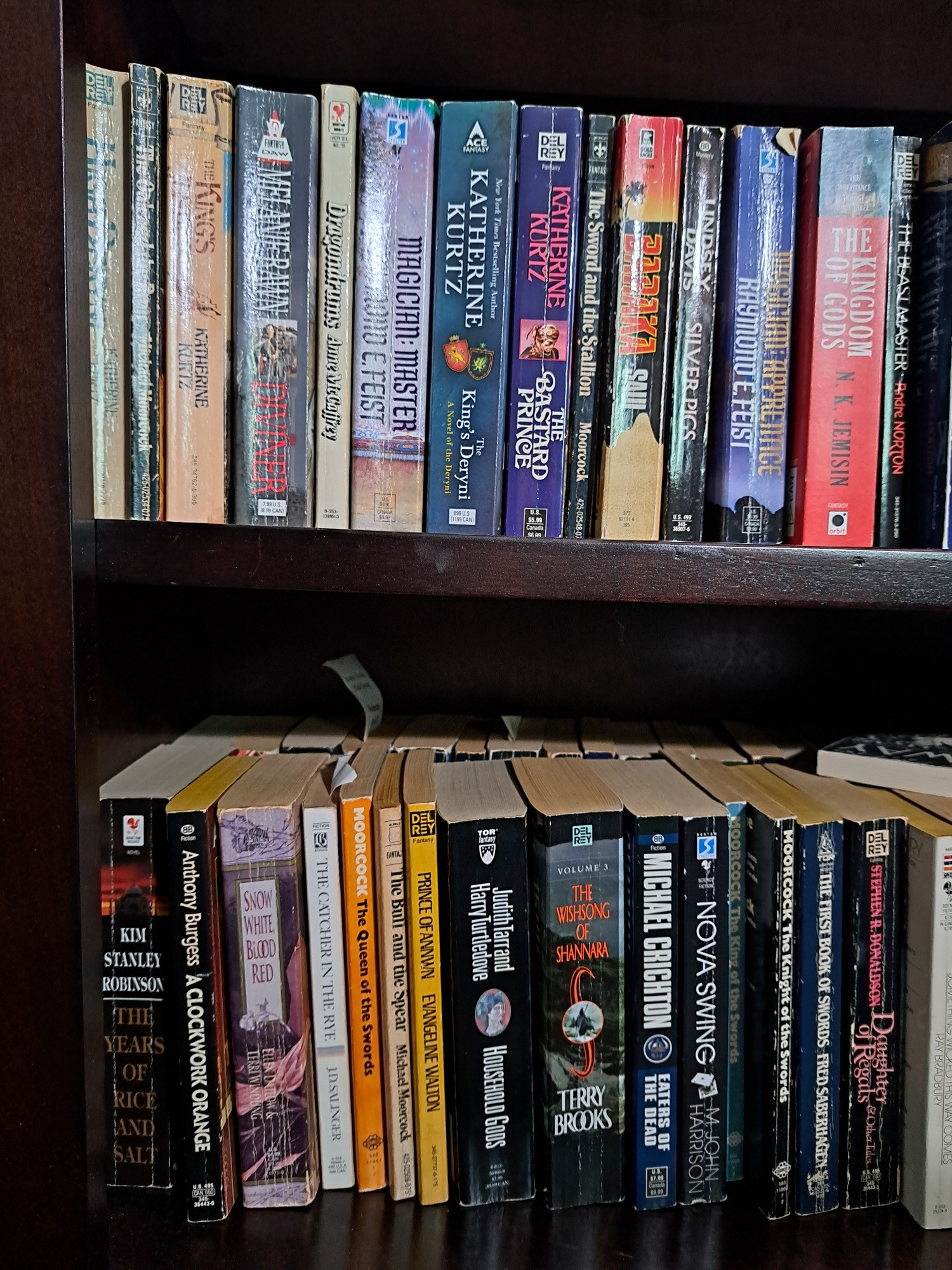 Two shelves of a taller bookshelf, shelves are double stacked with mass market paperbacks