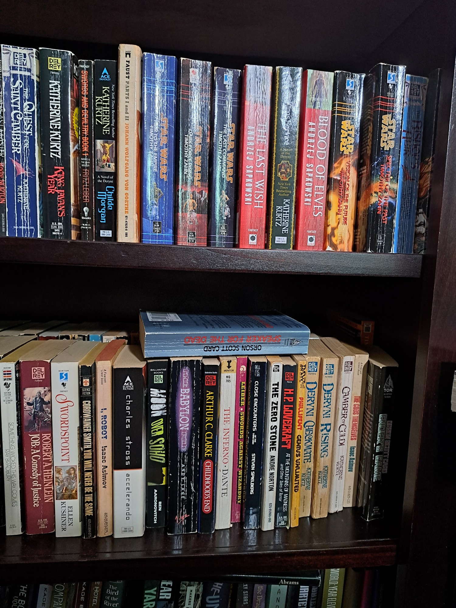 Two shelves of a taller bookshelf, shelves are double stacked with mass market paperbacks 
