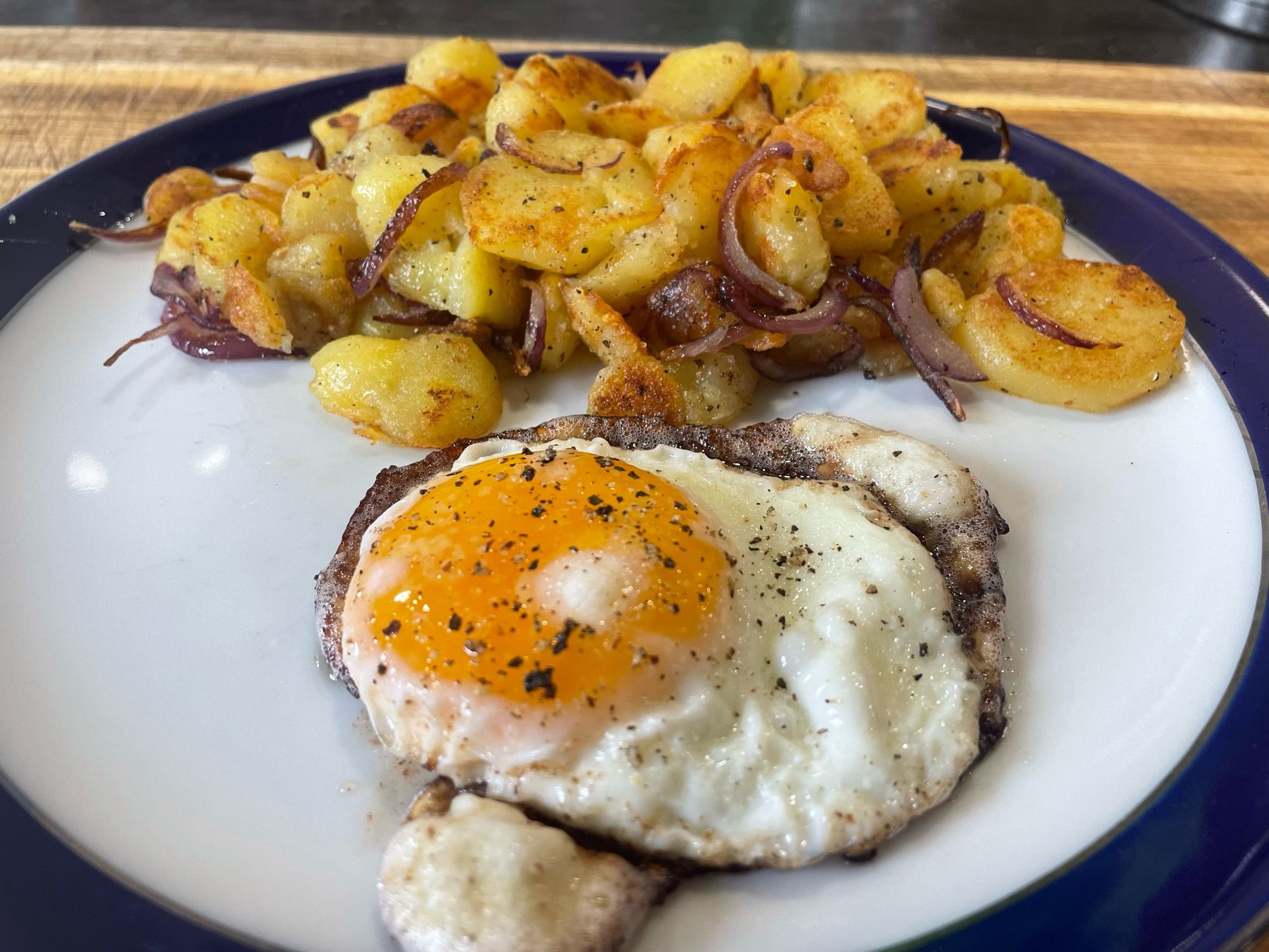 Bratkartoffeln mit roten Zwiebeln und Ei kross gebratenes Spiegelei.