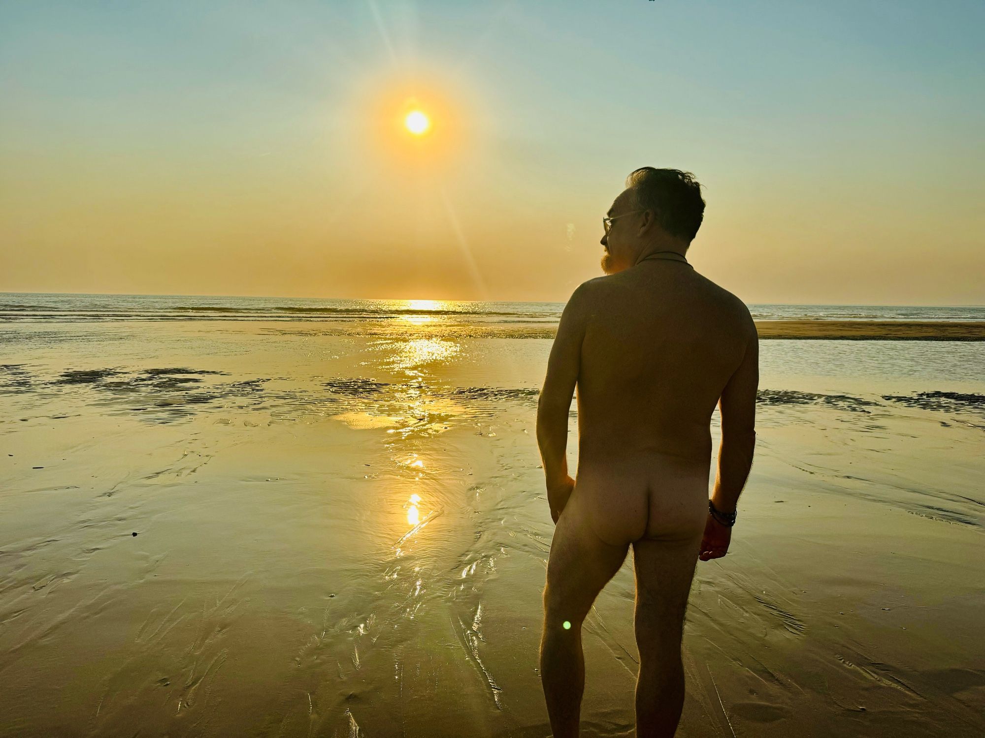 Naked Dad on the beach facing a sunset over the ocean (butt visible).