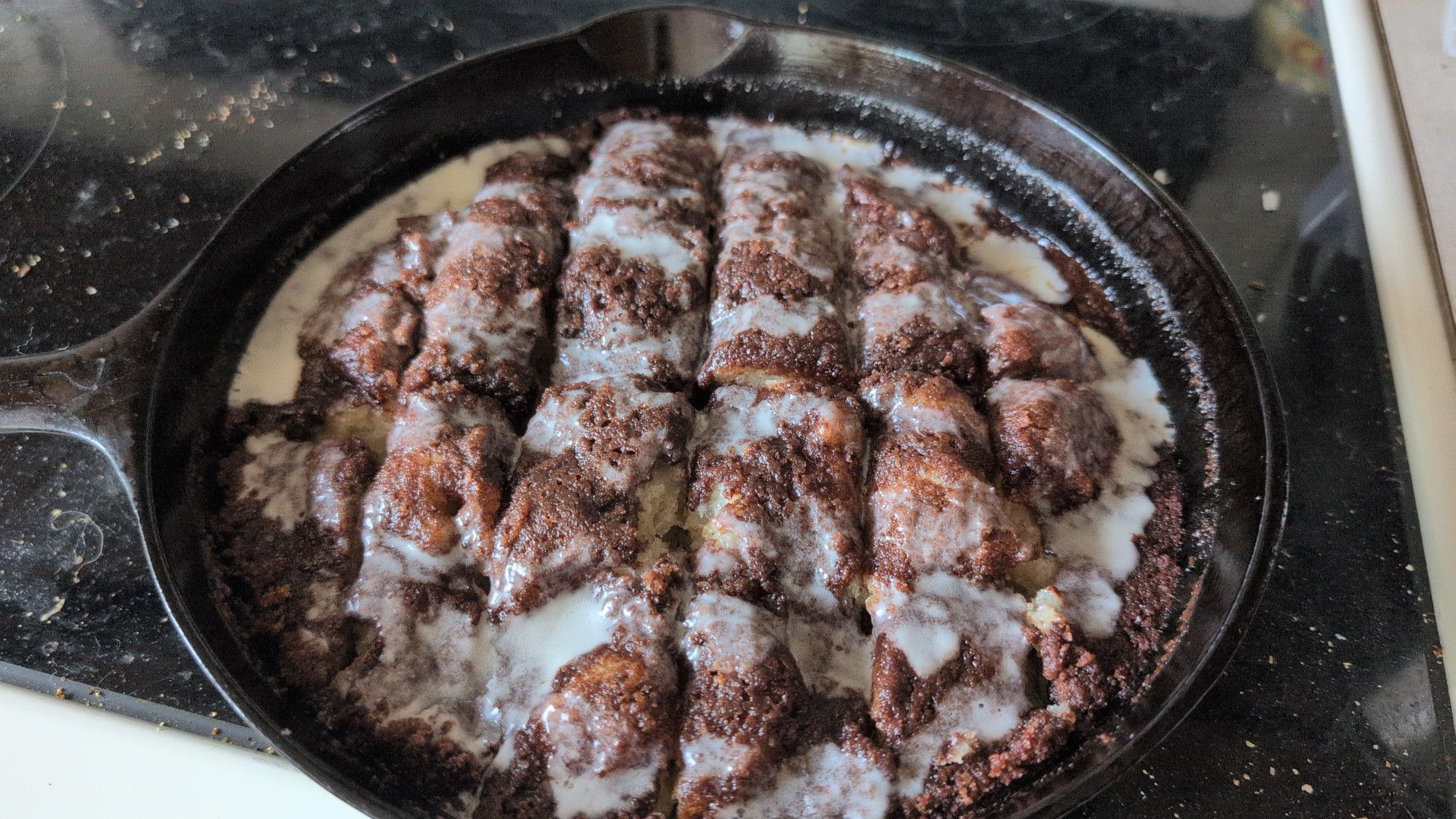 A cast iron pan full of pizza dough baked under a layer of cinnamon sugar compound butter and drizzled with icing