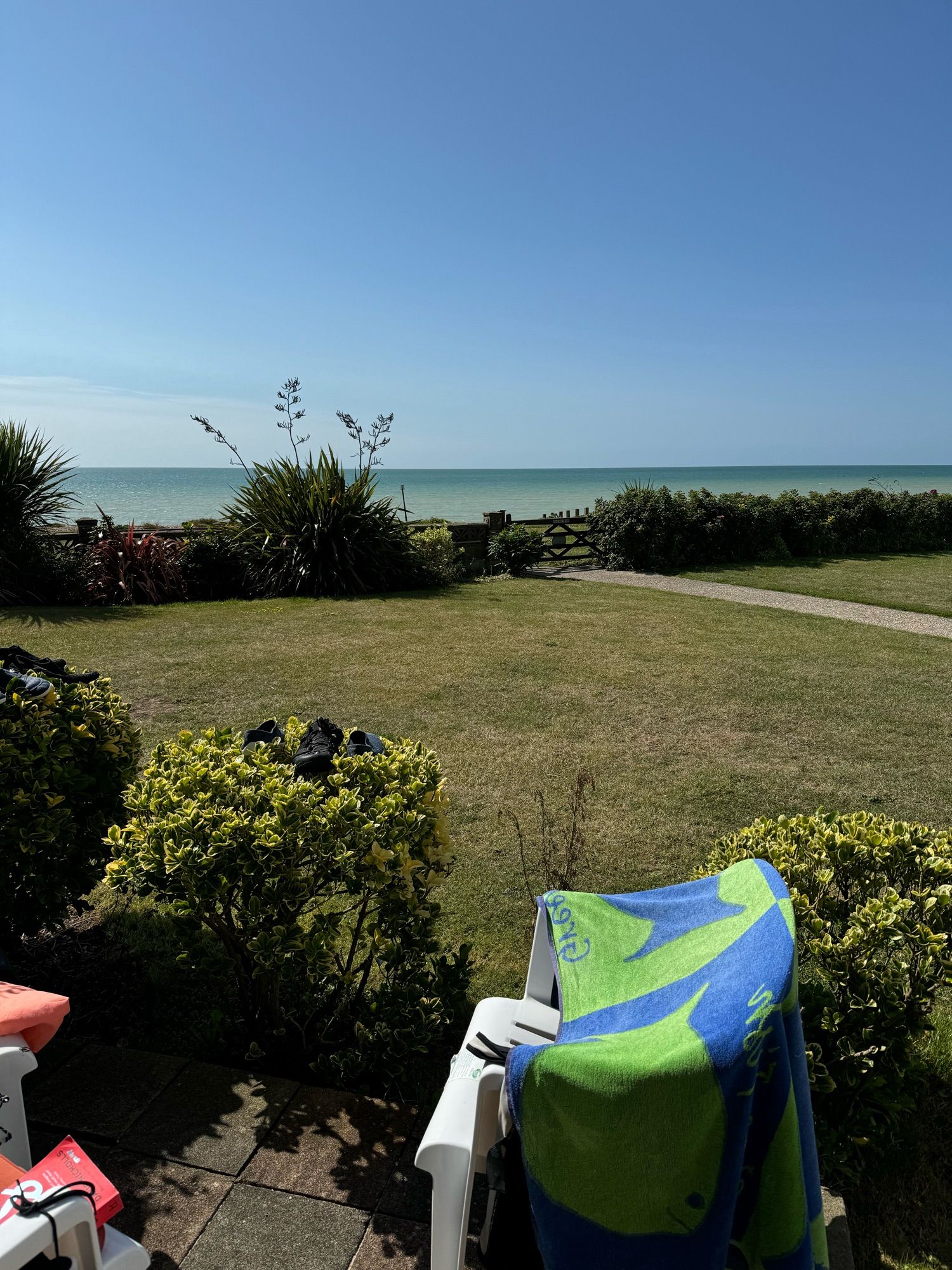 Towels and swimwear drying on garden chairs with lawn and sea in the background