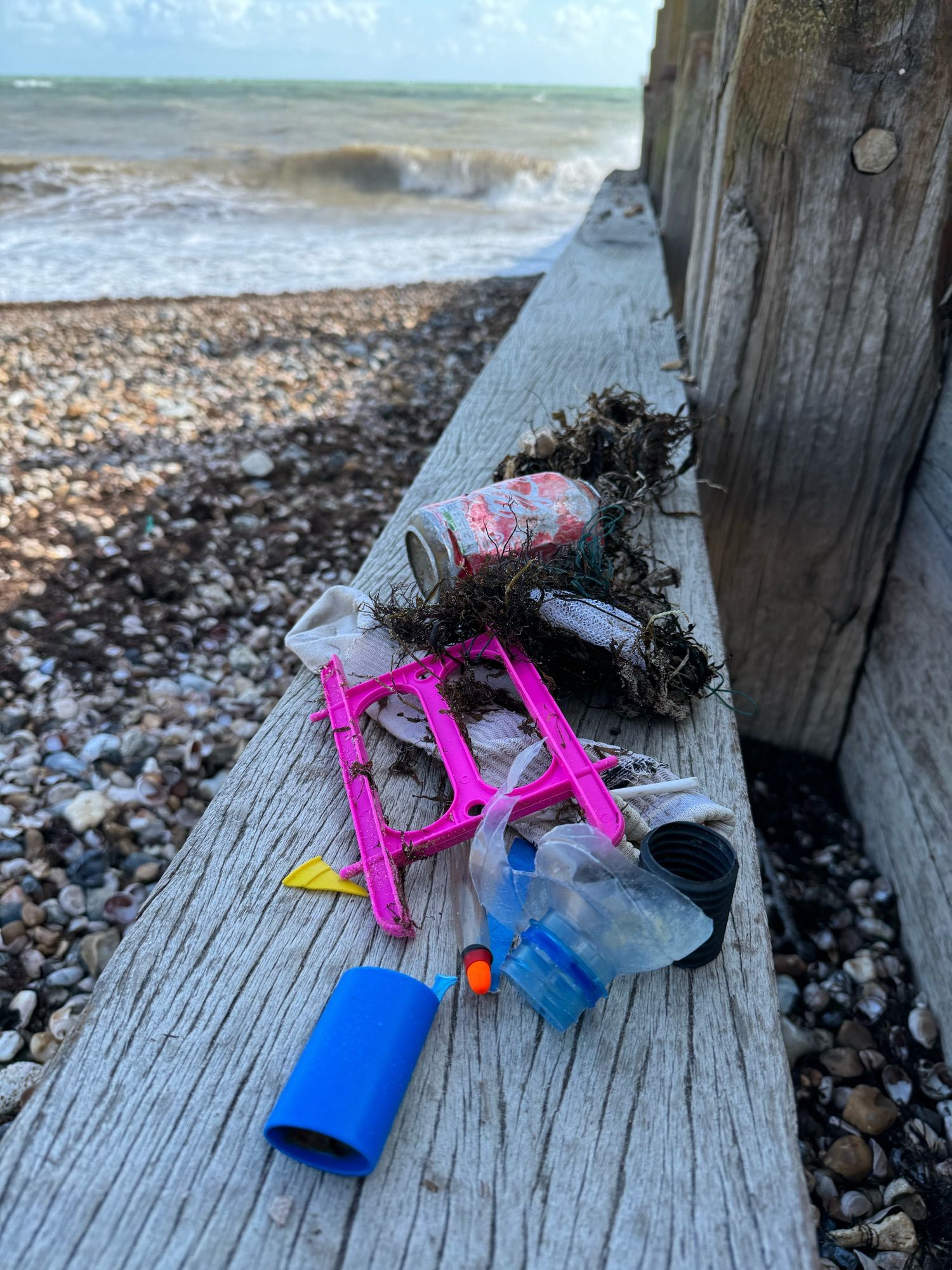 Items found during a beach clean including crab line, sock, coke can, plastic bottle neck, plastic straw with the sea in the background.