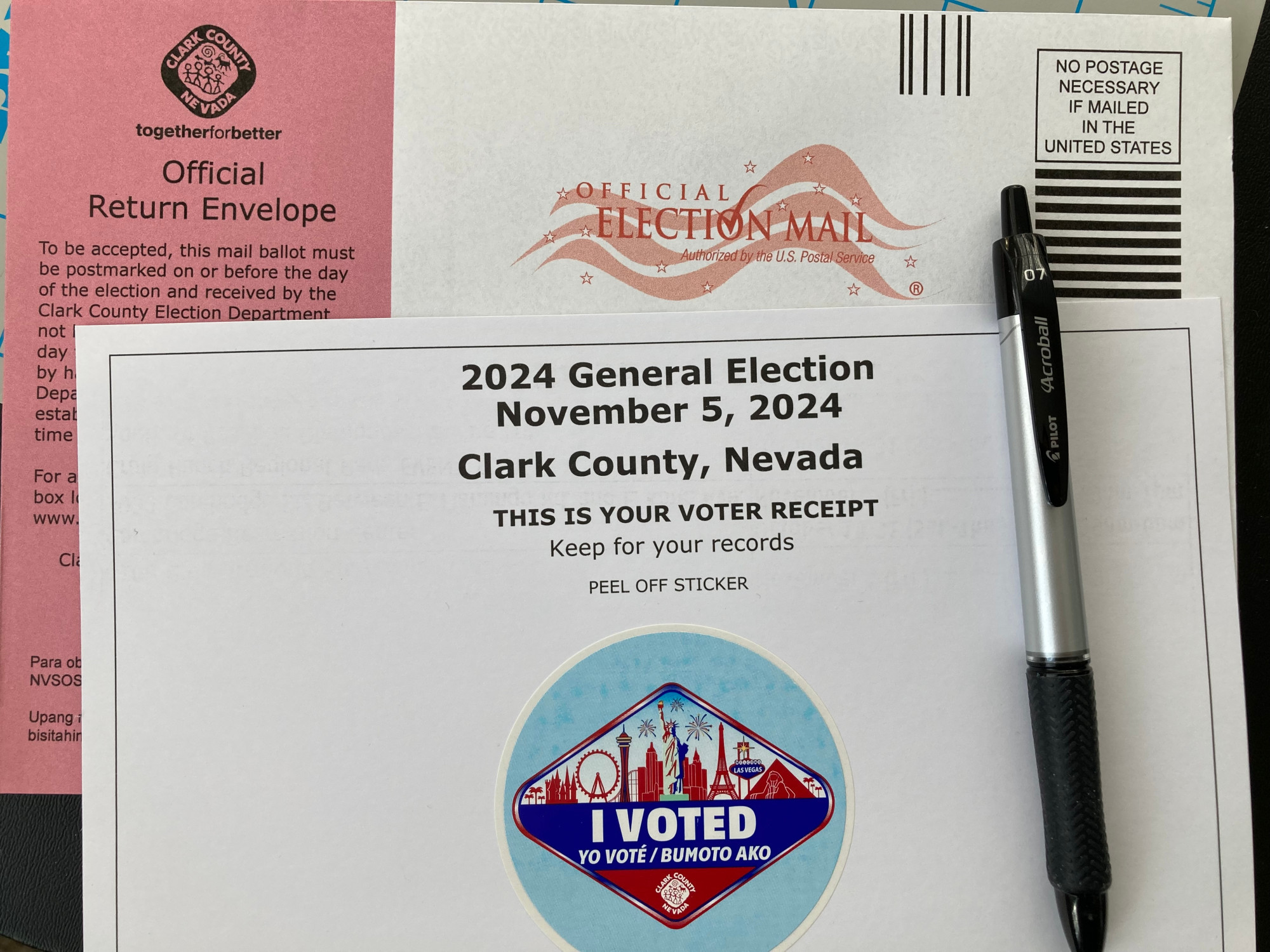 Mail-in ballot envelope and an "I VOTED" sticker. To the right sits a Pilot Acroball ballpoint pen.