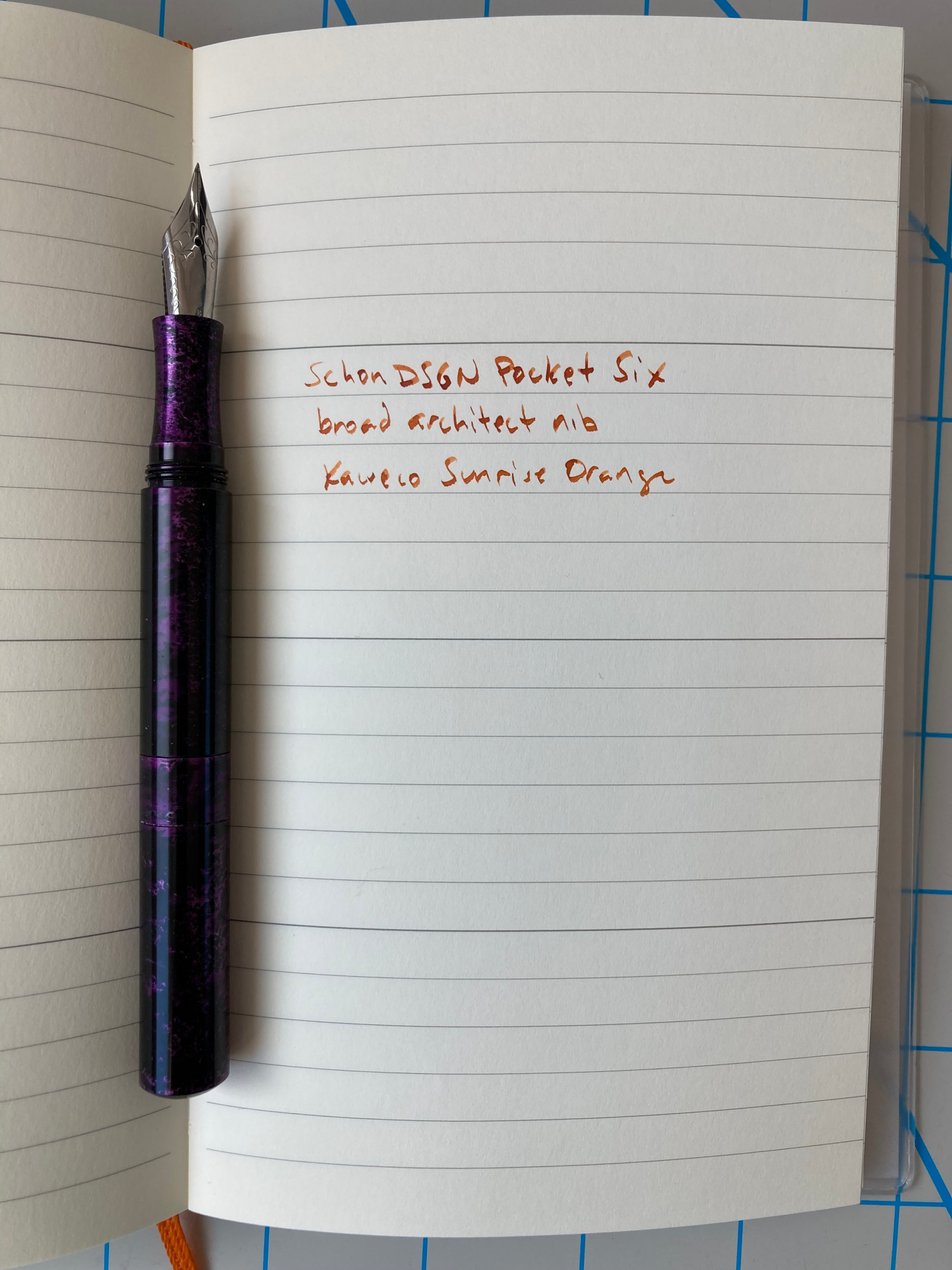 Written in a Midori MD notebook: "Schon DSGN Pocket Six, broad architect nib, Kaweco Sunrise Orange". The purple Schon DSGN pen sits to the left.