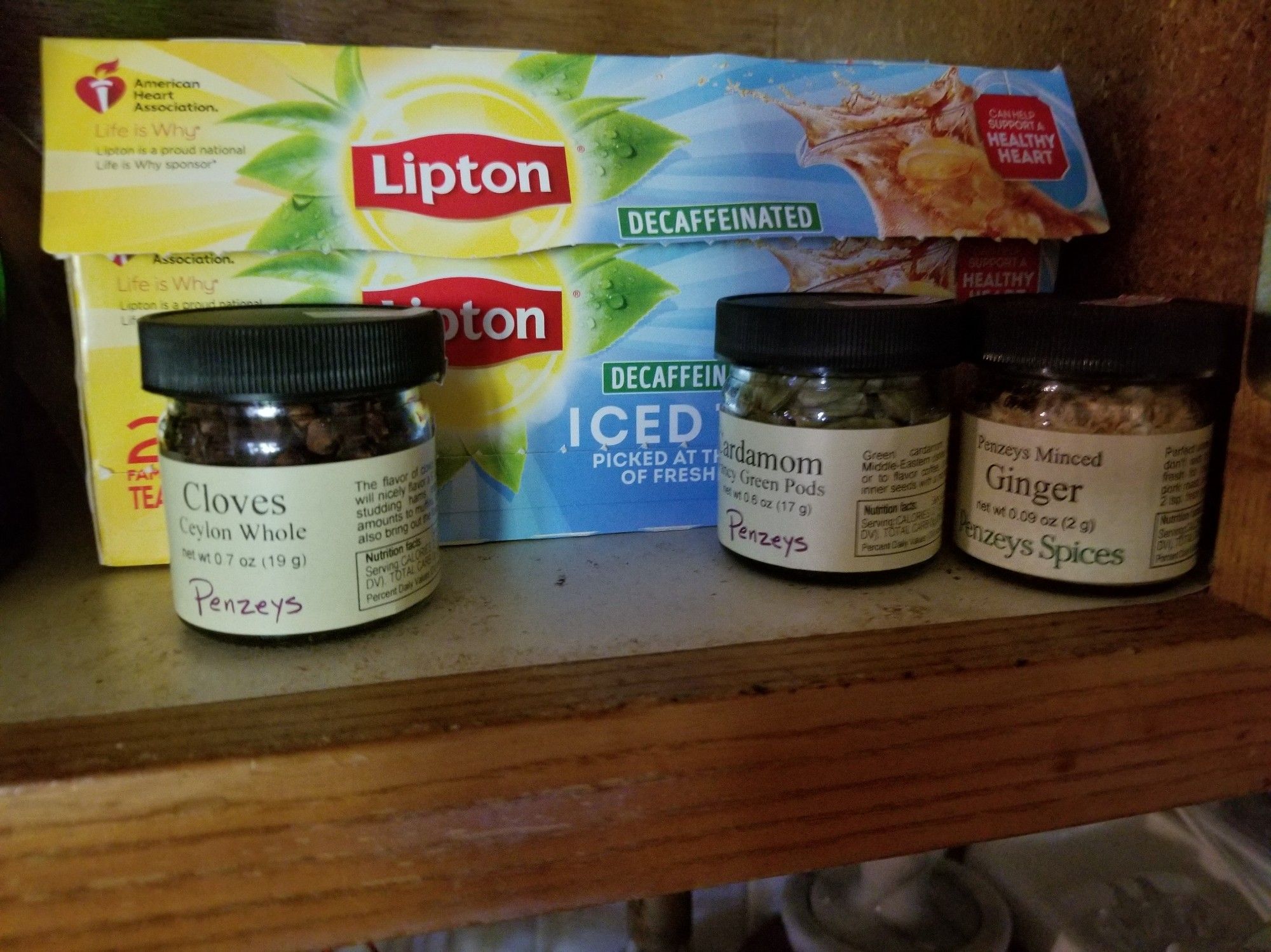 Three small Penzey's spice jars in front of a box of tea bags.