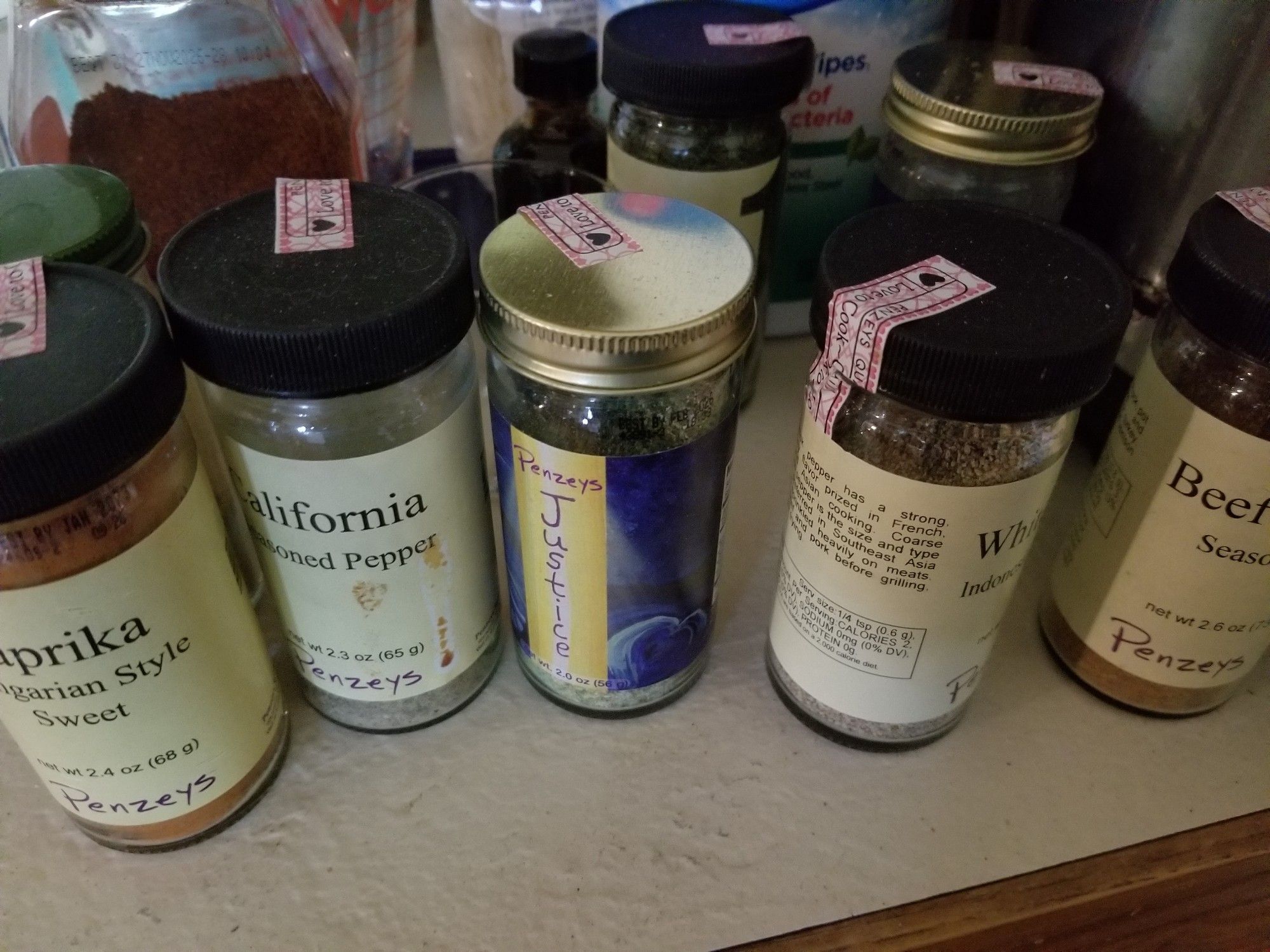 Seven jars of Penzey's spices on a counter.