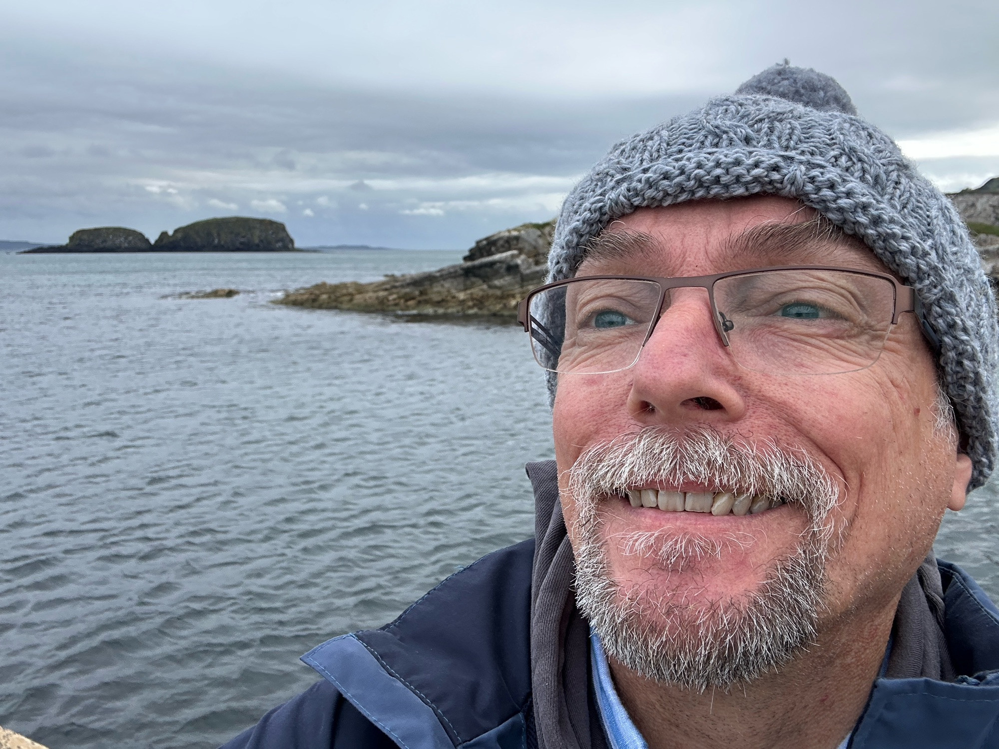 Middle aged man in woolly hat on the coast of Northern Ireland with Sheep Island in the background