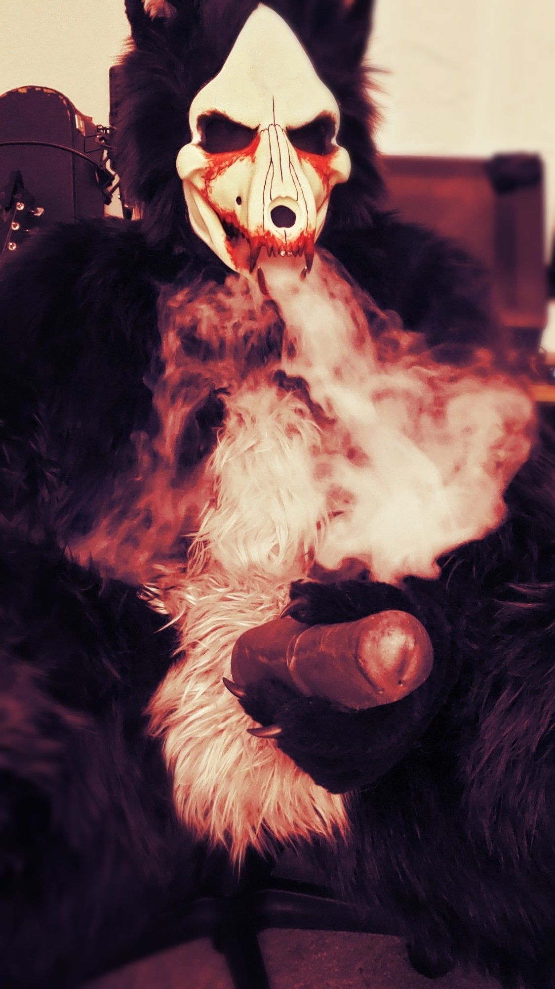 A skulldog with blood on his face, large and fluffy, leaning back while smoke pours from his mouth, running his body. He has a huge horsecock between his legs that he's holding in his hand, pointing toward the viewer. Light gleams off the head.