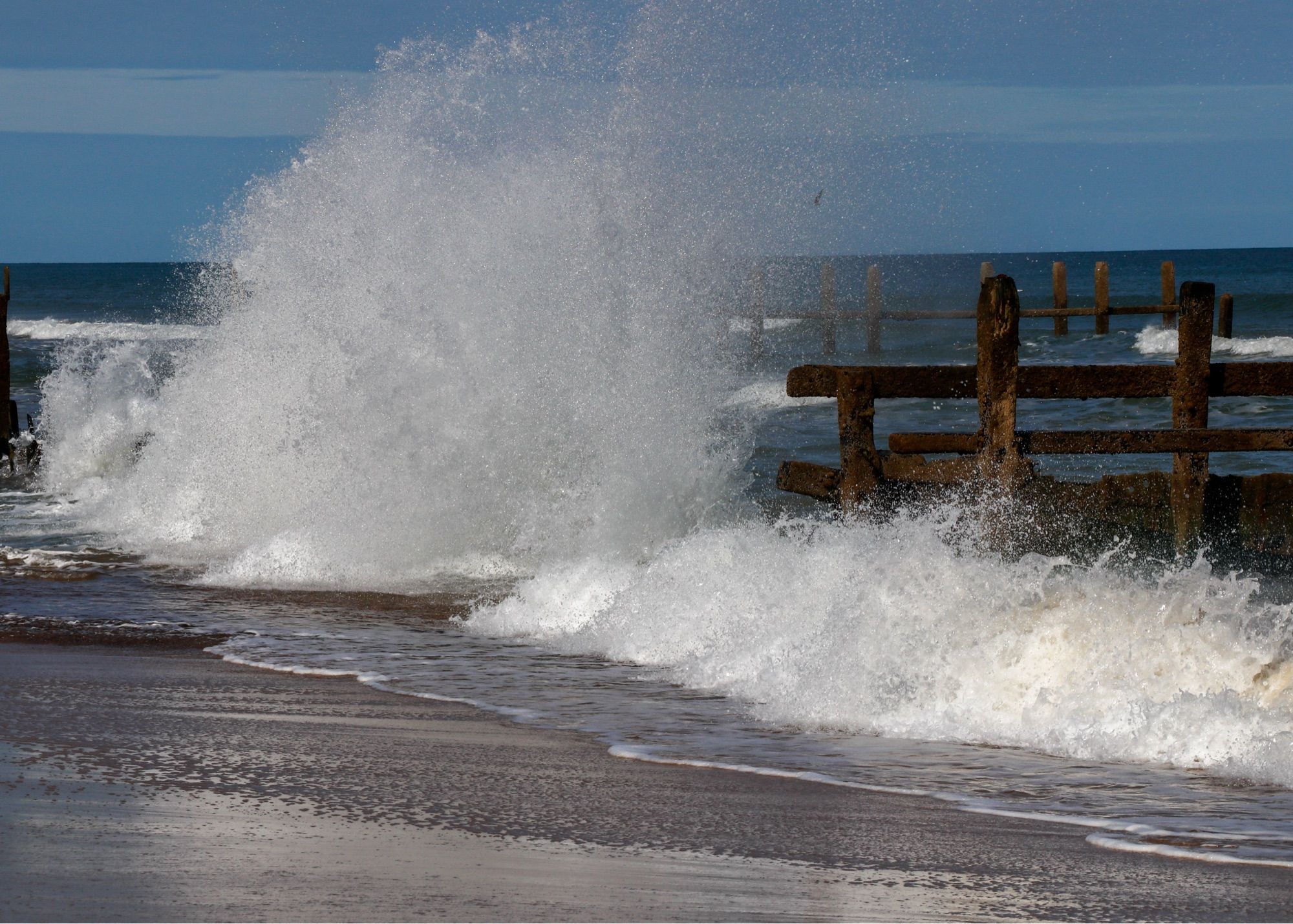 A huge plume of white spray crashing on to the beach after a wave has hit the sea defences