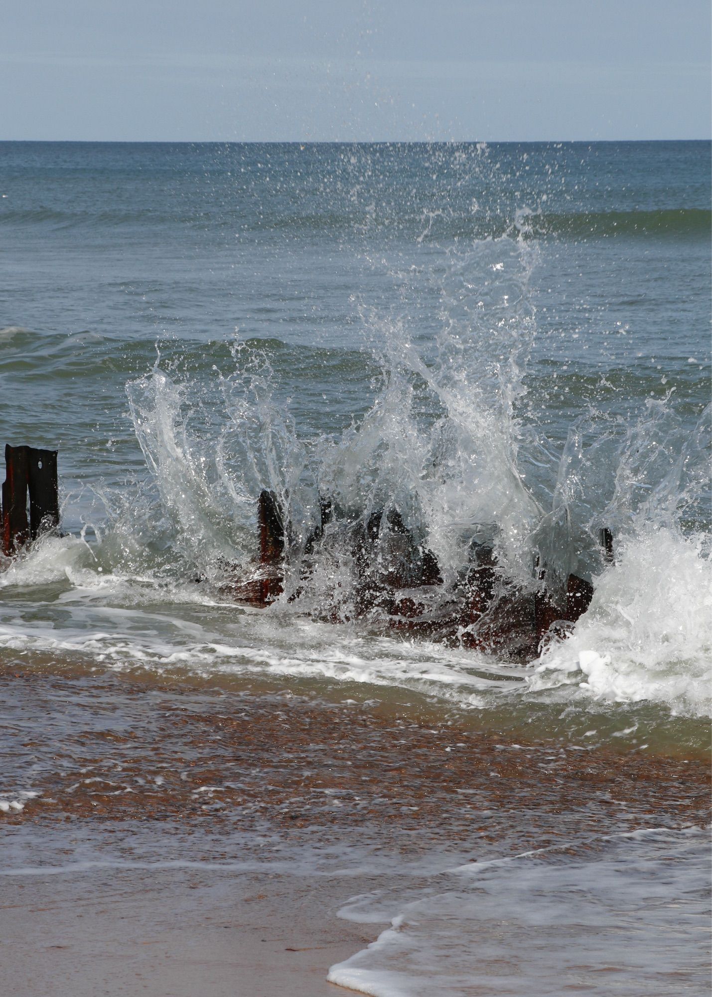 White spray from a wave reaching high into the air after hitting a beach defense