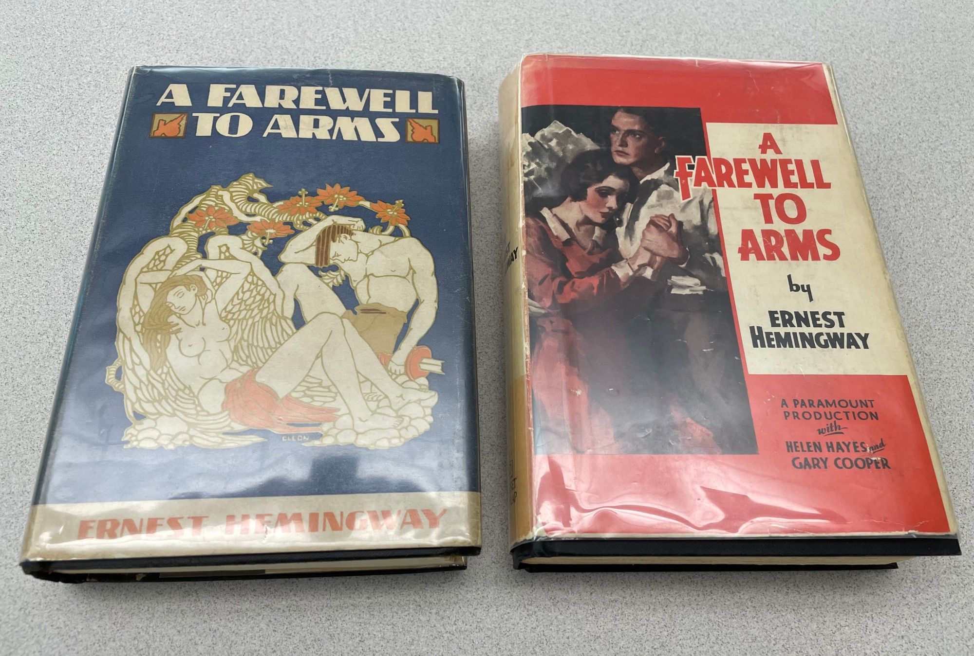 Two copies of Ernest Hemingway's A Farewell to Arms. Left is the first edition with an classical-inspired design of a man and angel reclining on the front; right is the reprint featuring the a man and woman in an embrace.