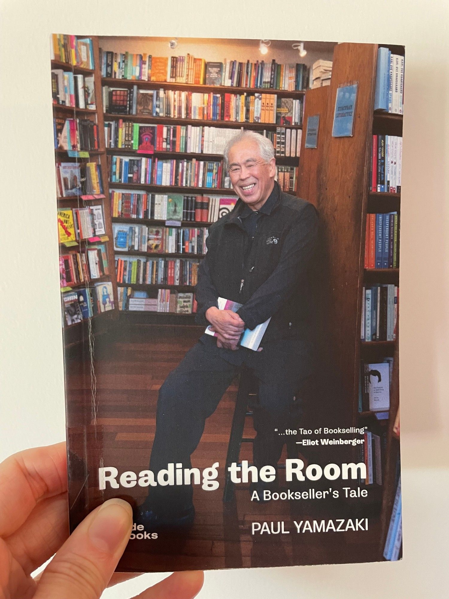 Cover of Paul Yamazaki's Reading the Room: A Bookseller's Tale, features Yamazaki seated in bookstore in front of shelves.