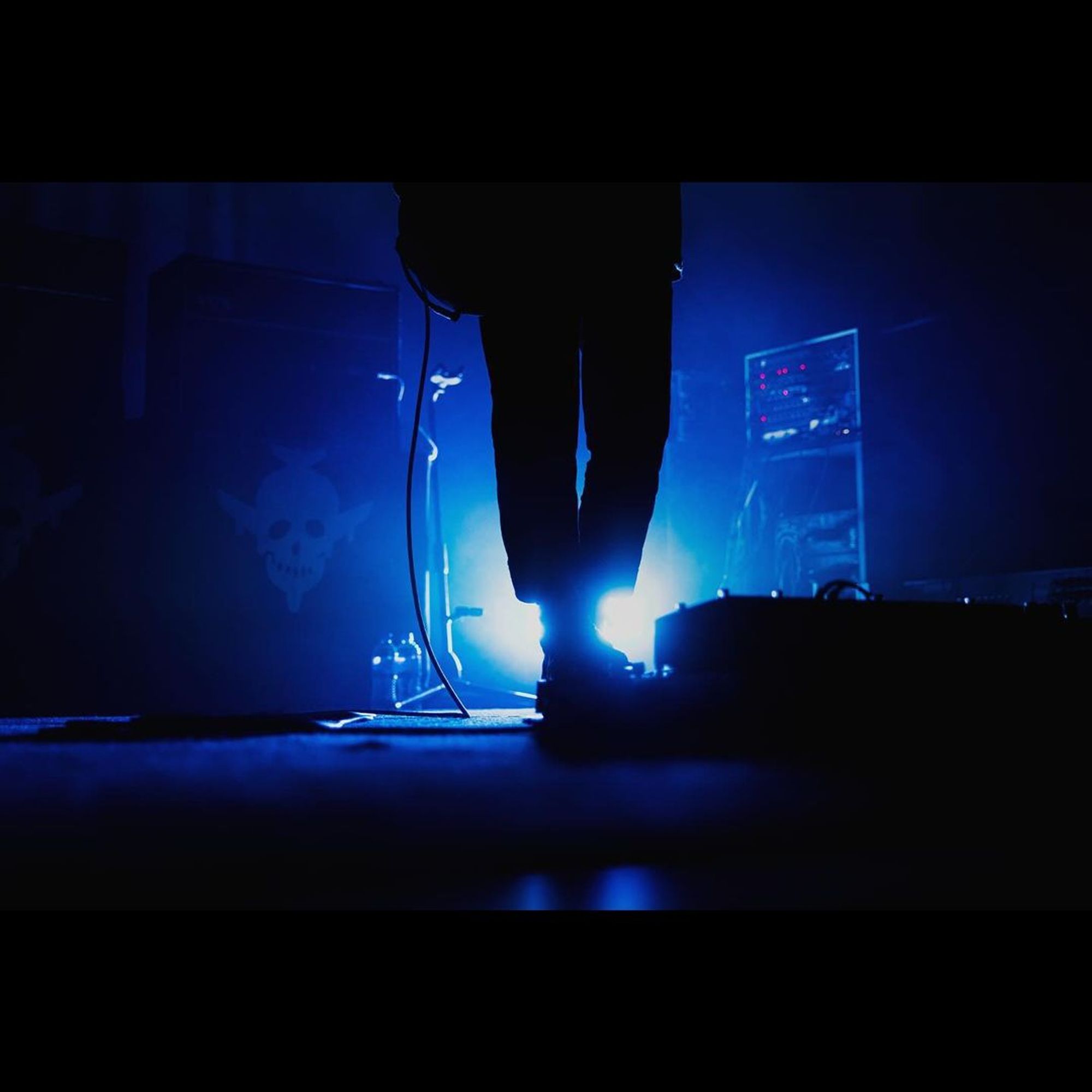 the shot is of Pete's feet at his pedal board, blue light peeks out behind him.