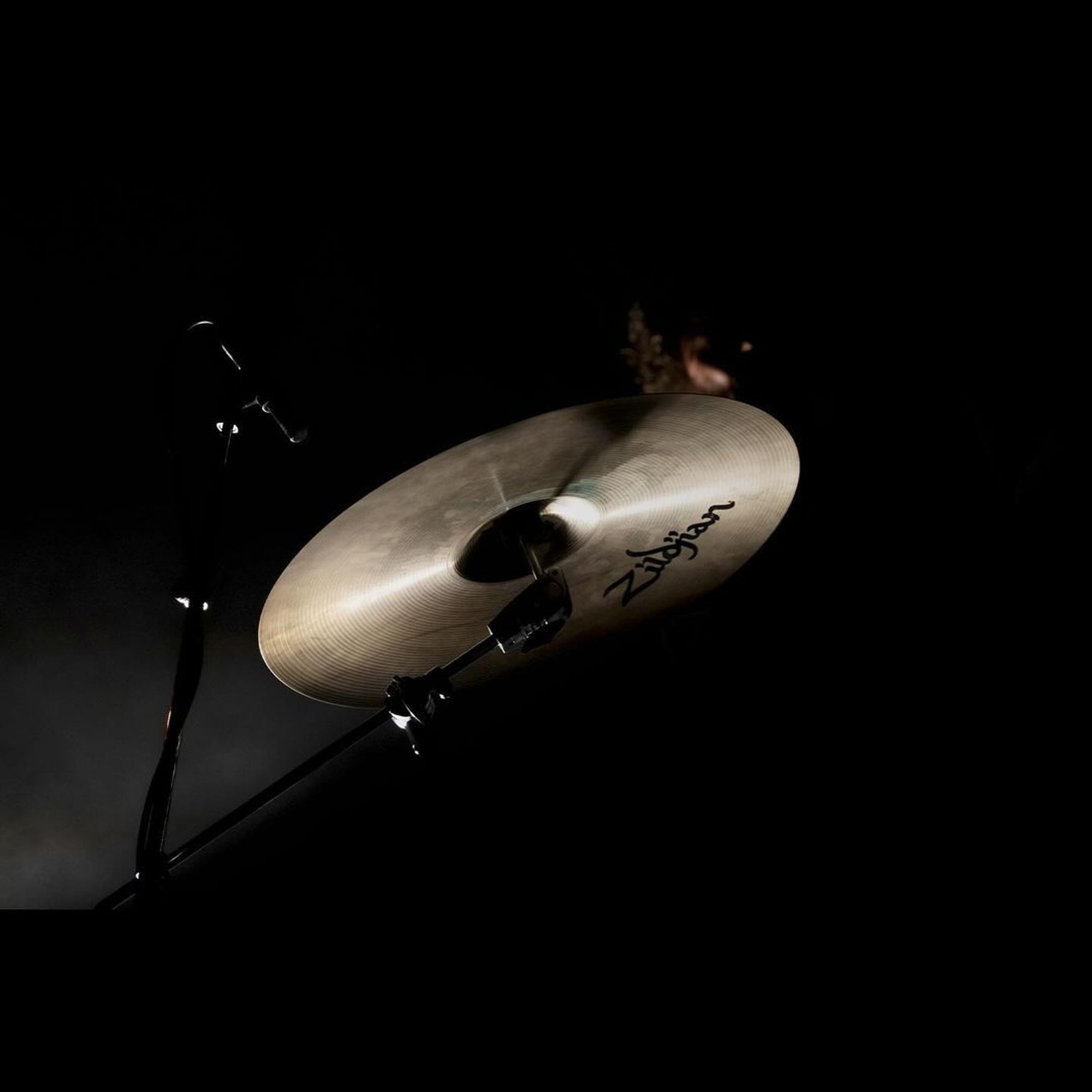 Brent in shadows, only his cymbal is illuminated.