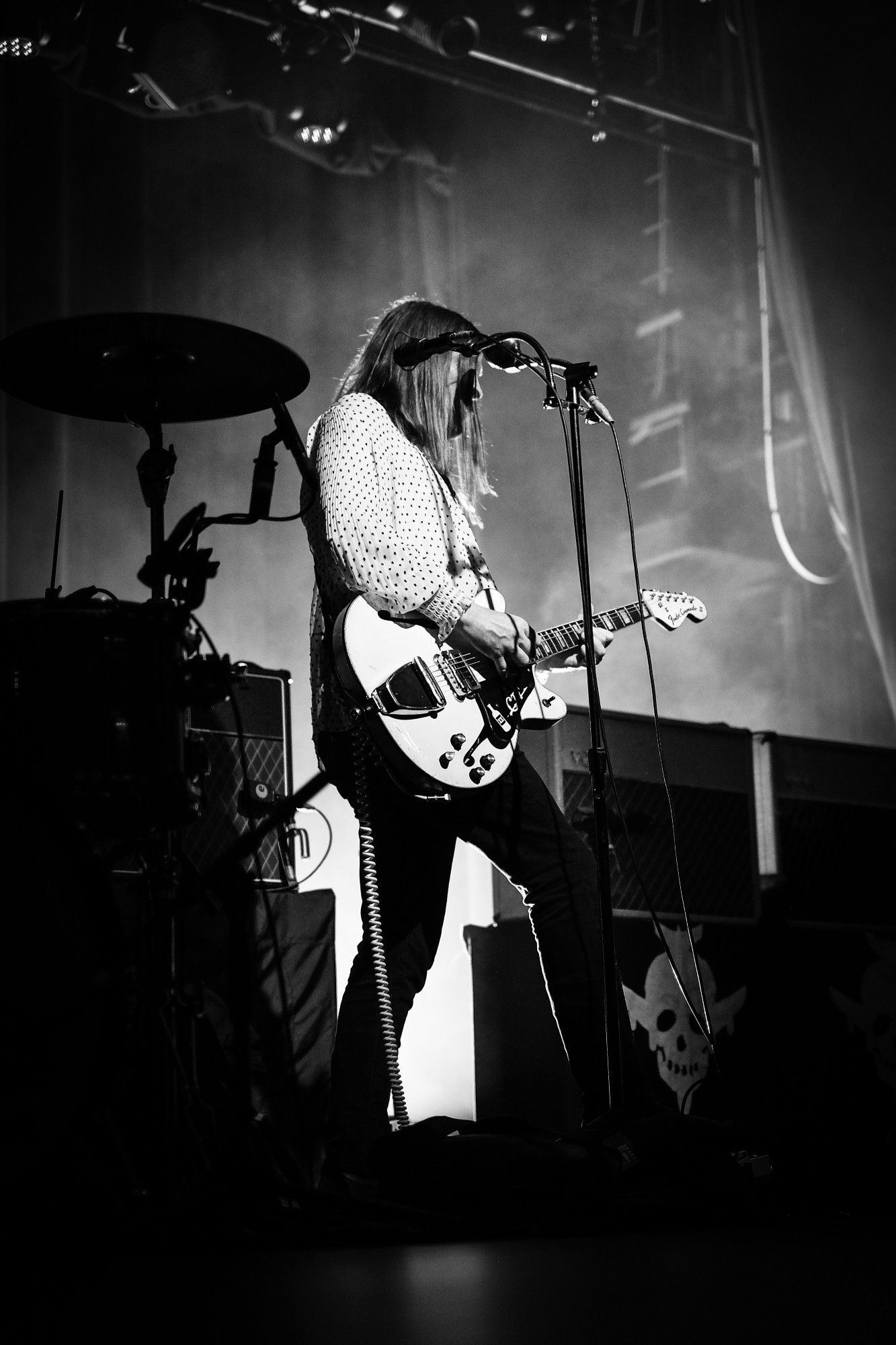 Black and white photo of Courtney on stage set back from his mic stand, playing his guitar.