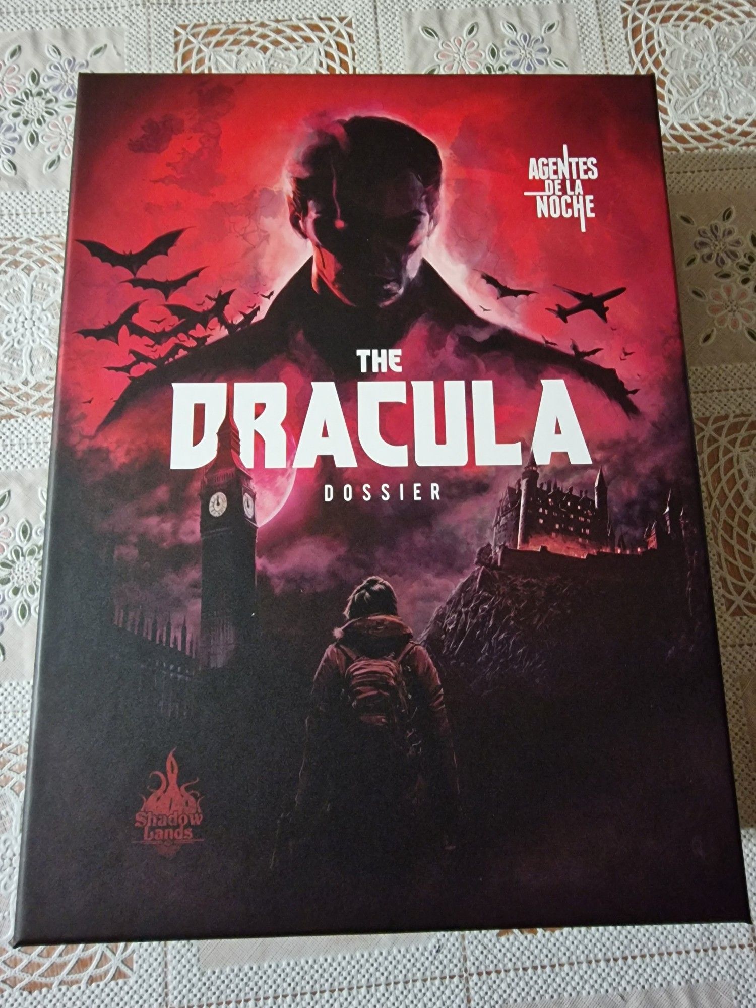 Portada de la caja The Dracula Dossier para Agentes de la noche. 
Caja en tonos de negro y rojo donde se ve en el fondo el busto de quien no puede ser otro que Drácula, saliendo murciélagos y un avión aún más al fondo. 

En primer plano varias localizaciones (un reloj que podría ser Big Ben y un castillo, quizás el del propio Drácula). 

Y en primer plano una persona de espaldas, probablemente mujer joven o adolescente con una mochila a la espalda.