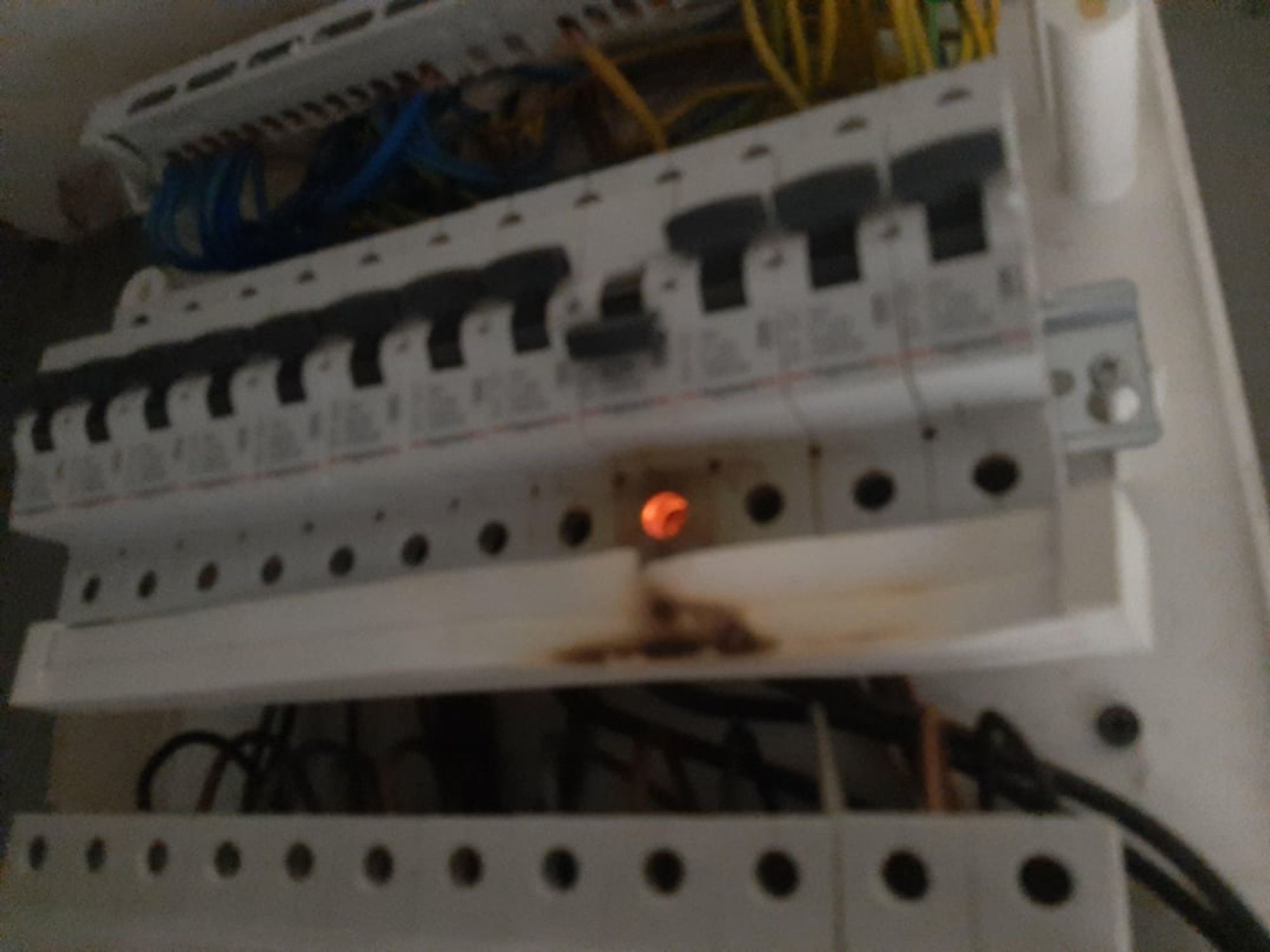 A breaker panel. One of the breakers is flipped and there are some scorch marks on the plastic housing below it. The hole below the flipped breaker is also glowing an ominous shade of amber.