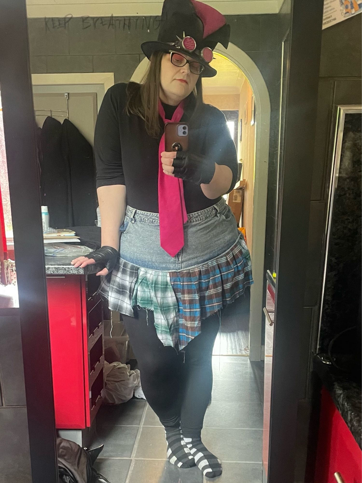 Stephanie Sterling in black top, pink tie, pink/black top hat, black fingerless gloves, and a skirt that’s denim on the top half and flannel cutoffs on the bottom.