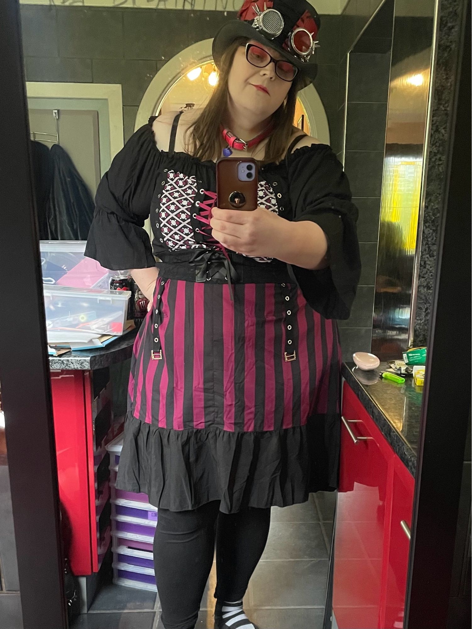 Stephanie Sterling mirror selfie, wearing red/black corseted top hat with goggles, and a sorta steampunky piratey dress that’s mauve and black with laces and a white/mauve diamond pattern up top, and a vertical line pattern past the waist. 

She looks great and will not accept sentiments to the contrary.