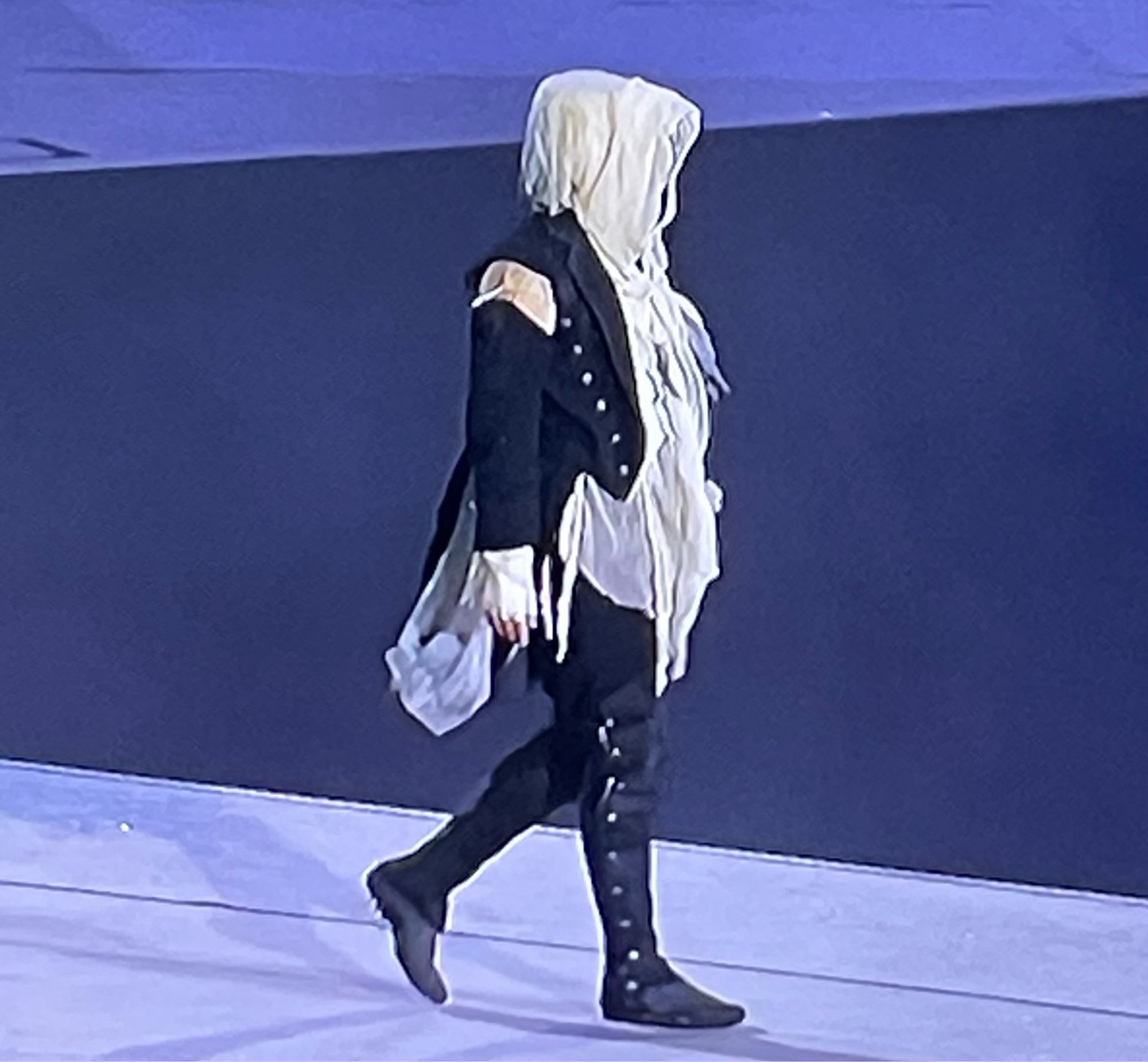 The individual, a sort of Assassins creed meets French Revolution meets ghost figure, in blue and white, walking down the runway at the paris Olympics closing ceremony