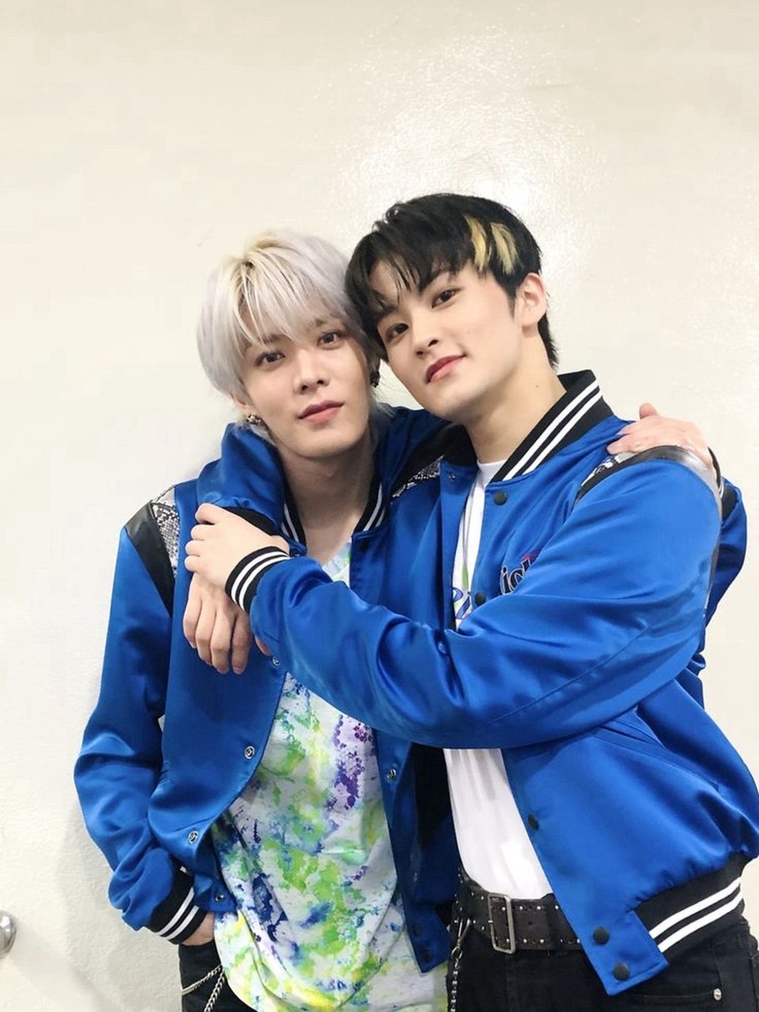 Mark and Yuta hugging backstage at a music show. They are wearing the blue jackets from Kick It era.