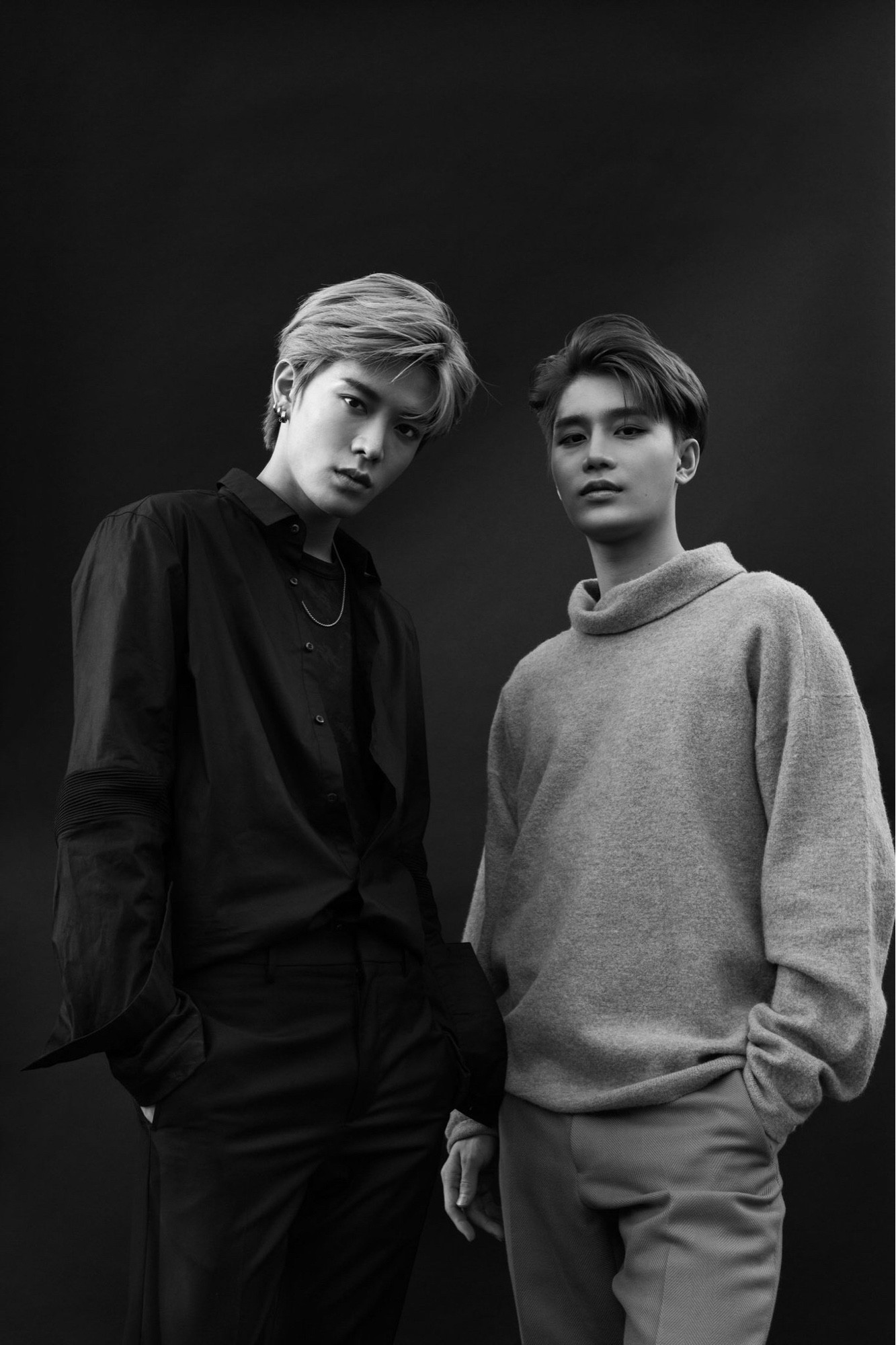 A black and white photoshoot picture of Yuta and Taeil standing with their hands in their pant pockets giving sultry looks to the camera.