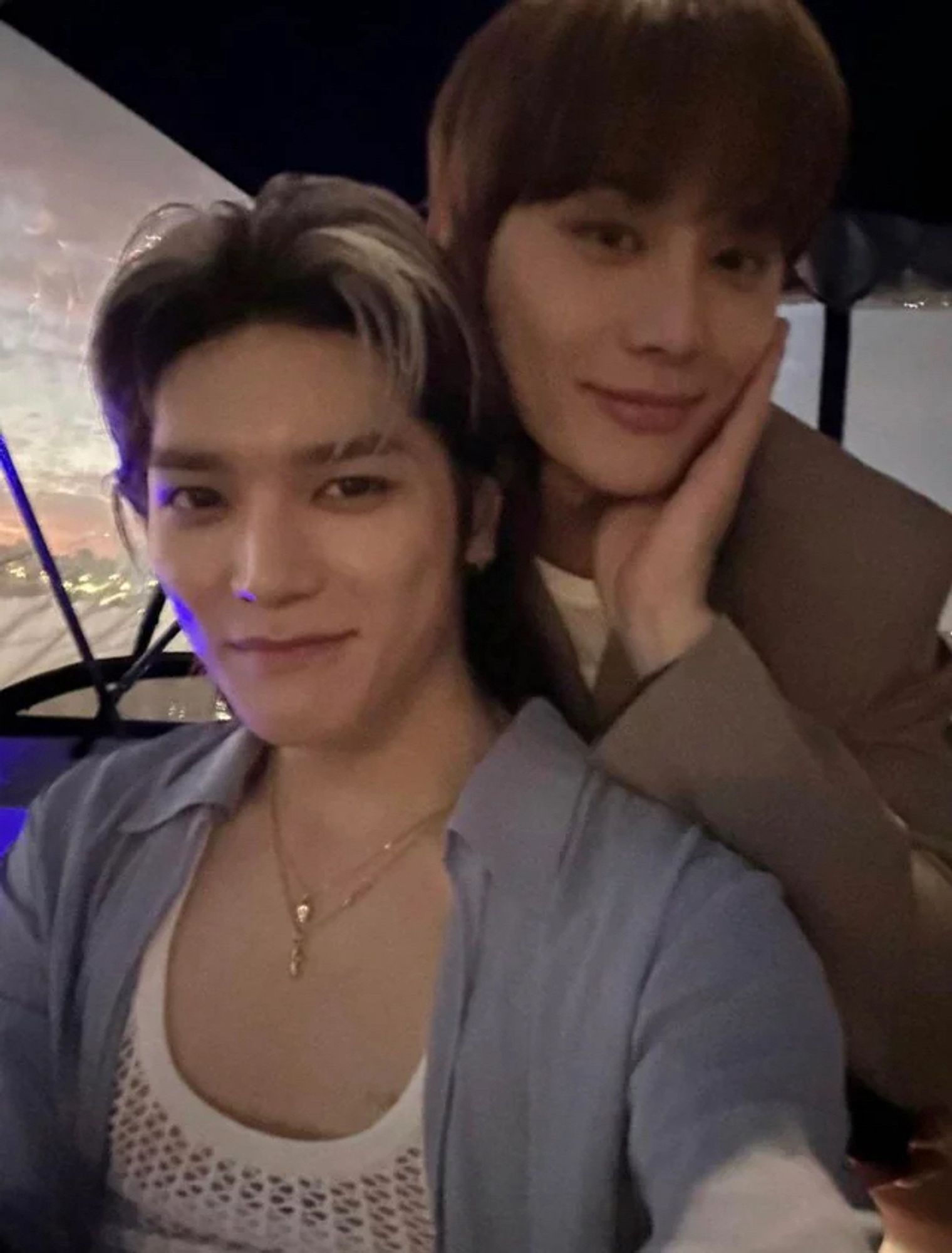 A selfie taken by Taeyong of him and Jungwoo on a boat. Jungwoo is standing behind Taeyong, with his head beside Taeyong’s head. Jungwoo is gently resting an open hand on his own cheek. He looks very demure. Taeyong looks like he’s about to burst out laughing.