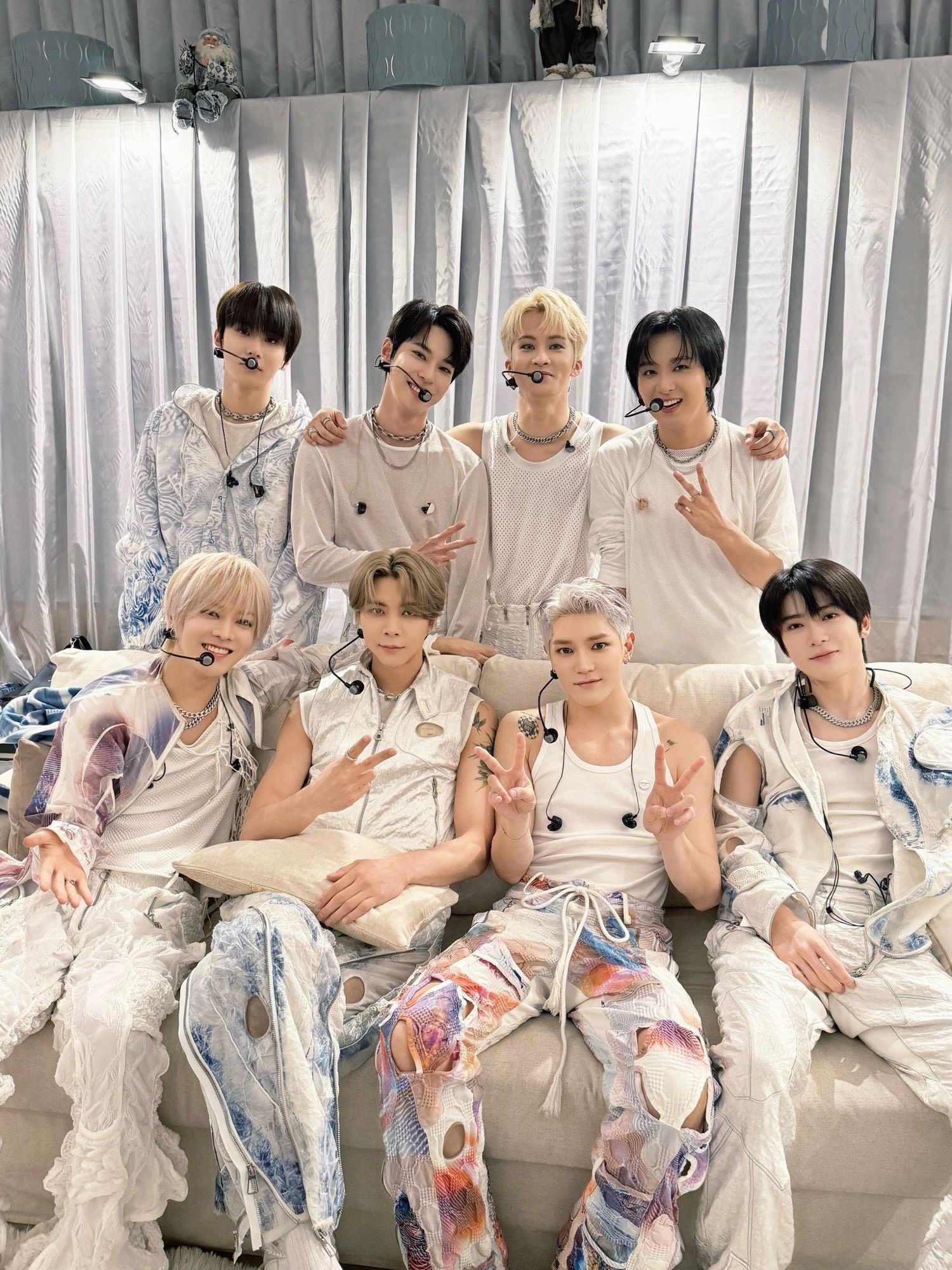 OT8 backstage in their white outfits before the start of a Unity Tour concert. Yuta, Johnny, Taeyong, and Jaehyun are sitting on a couch. Jungwoo, Doyoung, Mark, and Haechan are standing behind them.