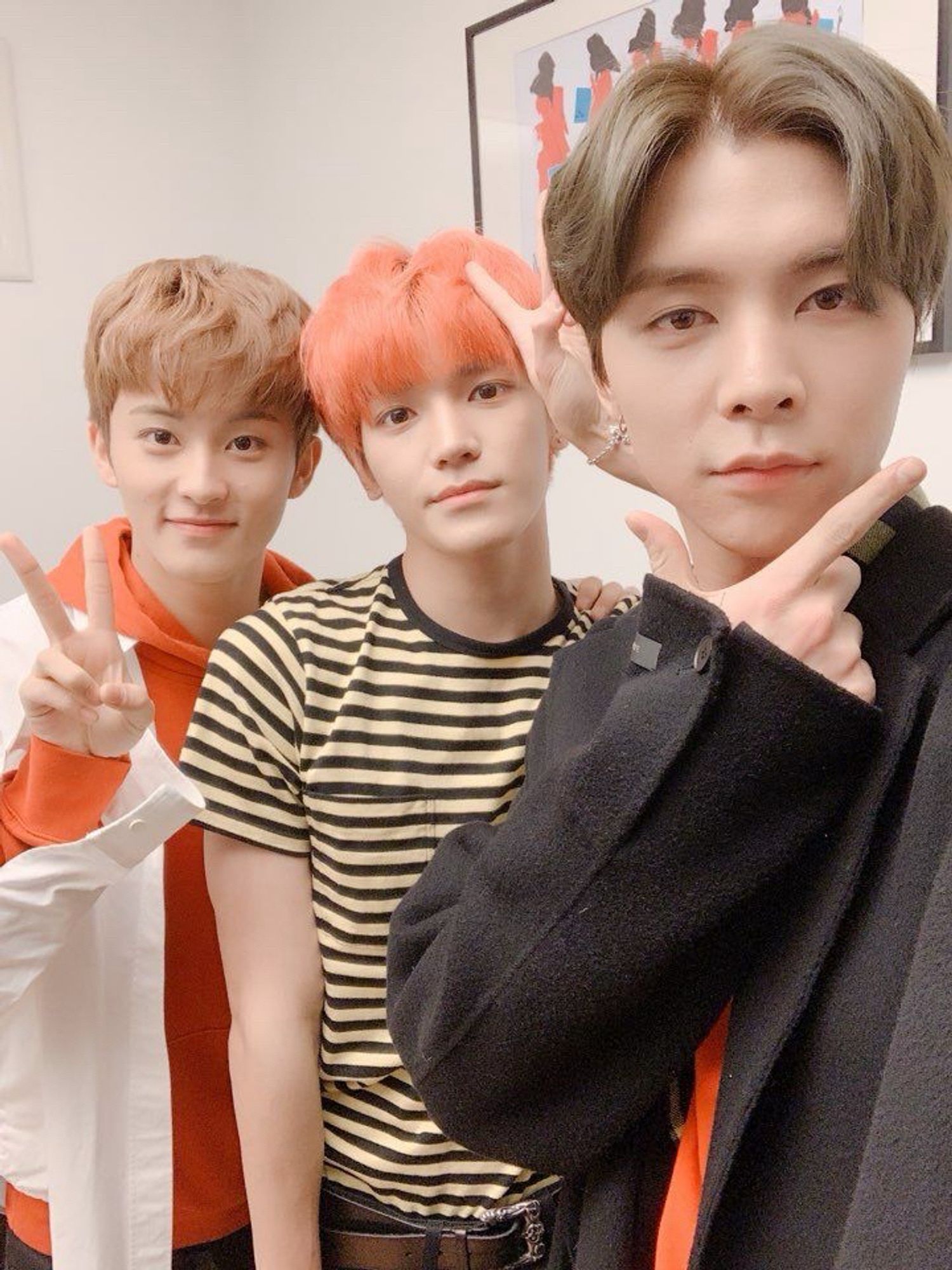 Very young, Taeyong, and Johnny. Mark is making a peace sign with one hand and has the other on Taeyong’s shoulder. Taeyong has pinkish-orange hair and is making a peace sign with one hand. Johnny is making an “L” with the thumb and pointer finger of one hand and has it under his chin.